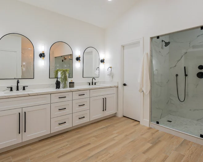 Bright modern bathroom with double vanity, arched mirrors, and glass walk-in shower.