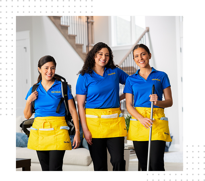 Three cleaning staff in blue and yellow uniforms standing with mops in a bright indoor lobby