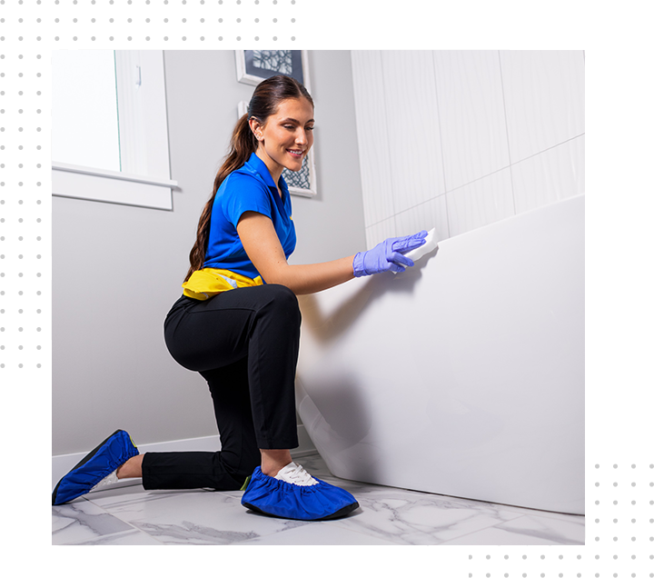 Cleaner in blue uniform scrubbing a white wall with a sponge, kneeling on a tiled floor