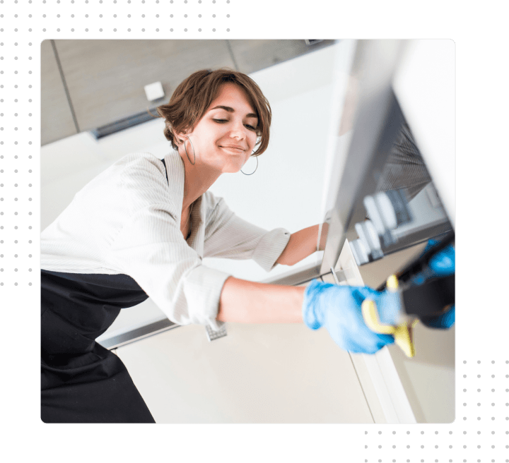 Smiling cleaner wiping a kitchen appliance with a blue cloth in a bright room