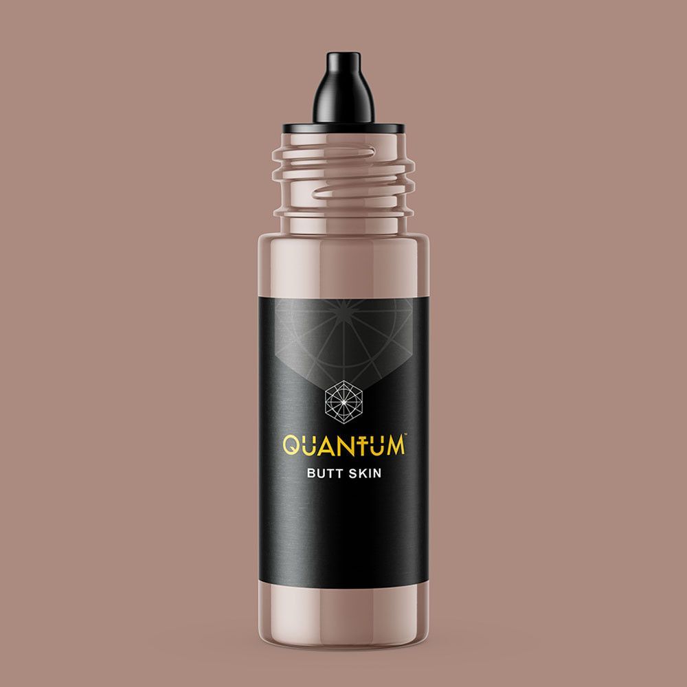 A bottle of Quantum brand tattoo ink, featuring a black label with gold text on a matching light brown background.