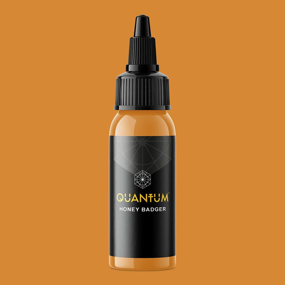 A bottle of Quantum brand tattoo ink in the color Honey Badger, featuring a black label with gold text on a white background.