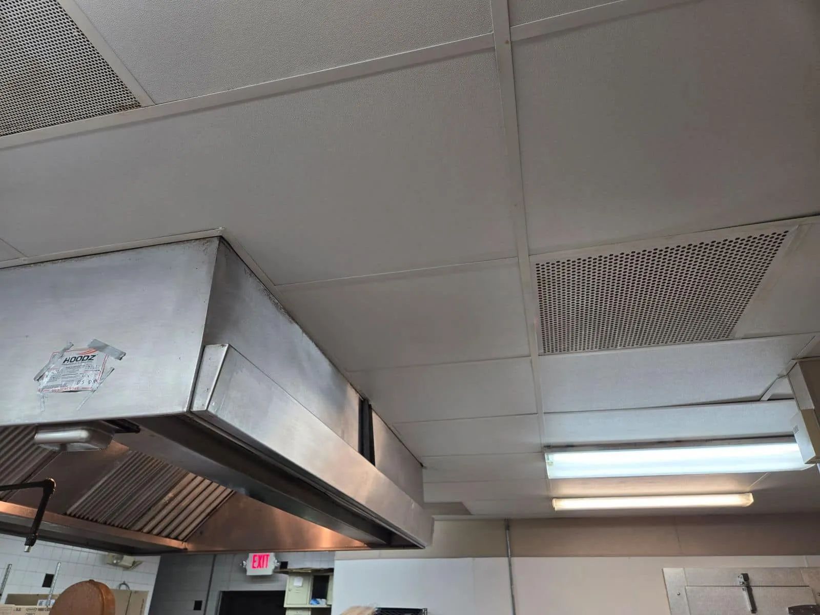 Commercial kitchen ceiling with stainless steel hood vents and fluorescent light panels