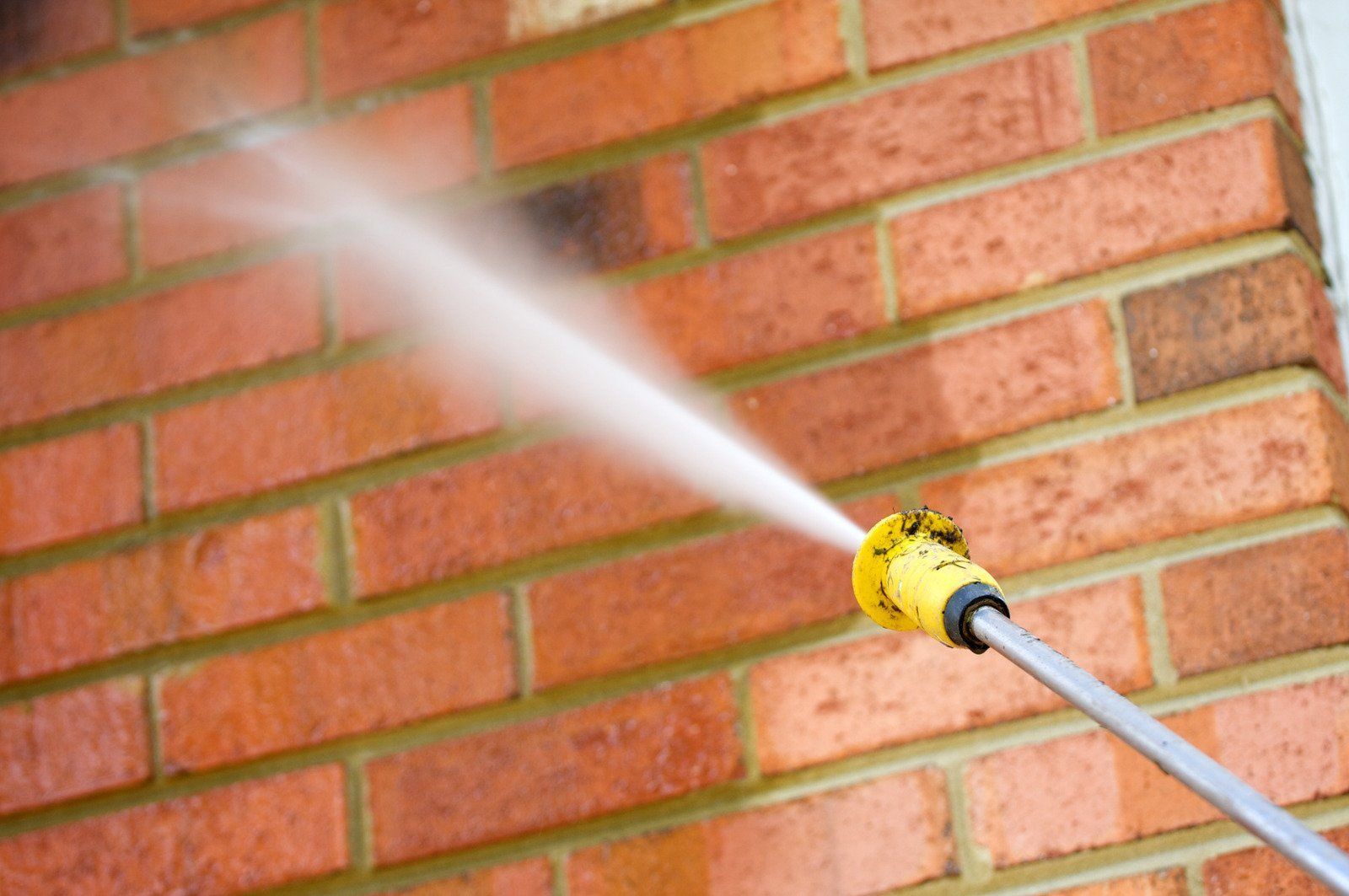 Pressure washer spraying a red brick wall.