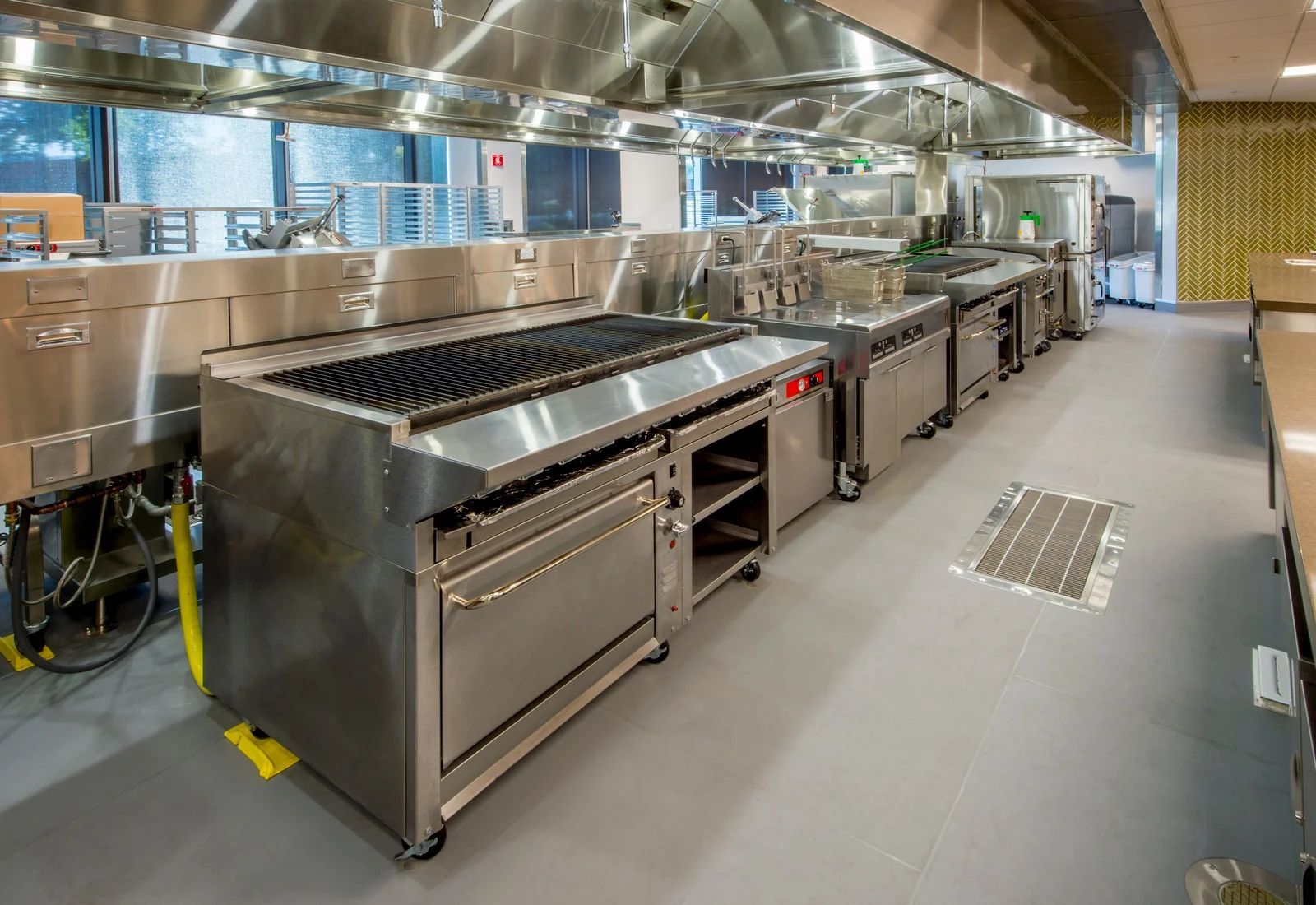 Large stainless steel commercial kitchen line with stovetops, ovens, and ventilation hood