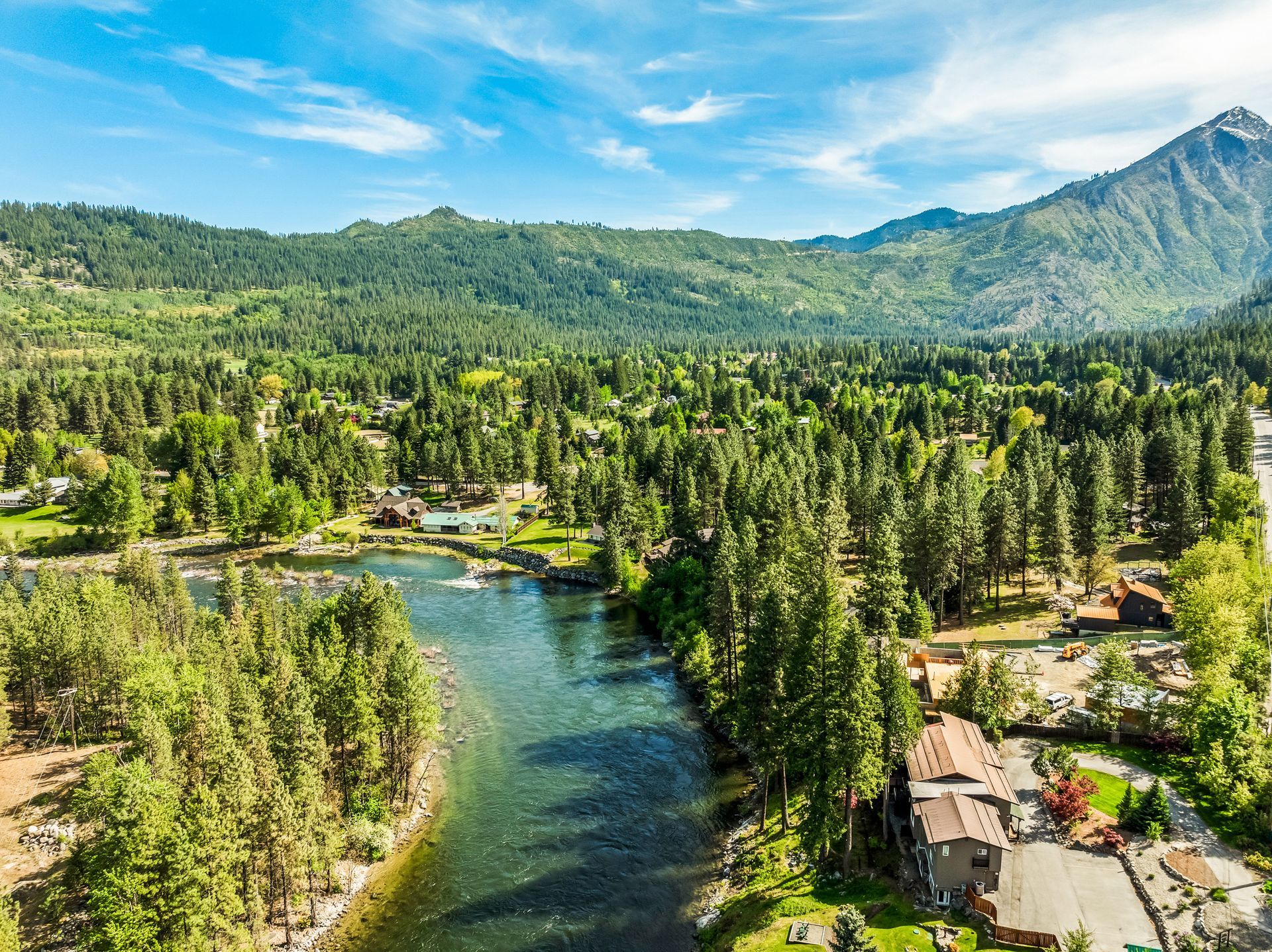 River flowing through a green forest, mountains in the background under a blue sky.