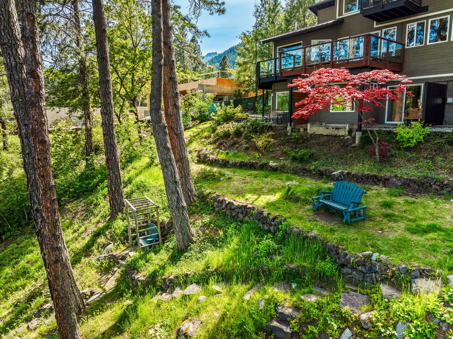 Boutique hotel with green lawn, trees, terraced garden, and a blue bench. Red tree stands out.