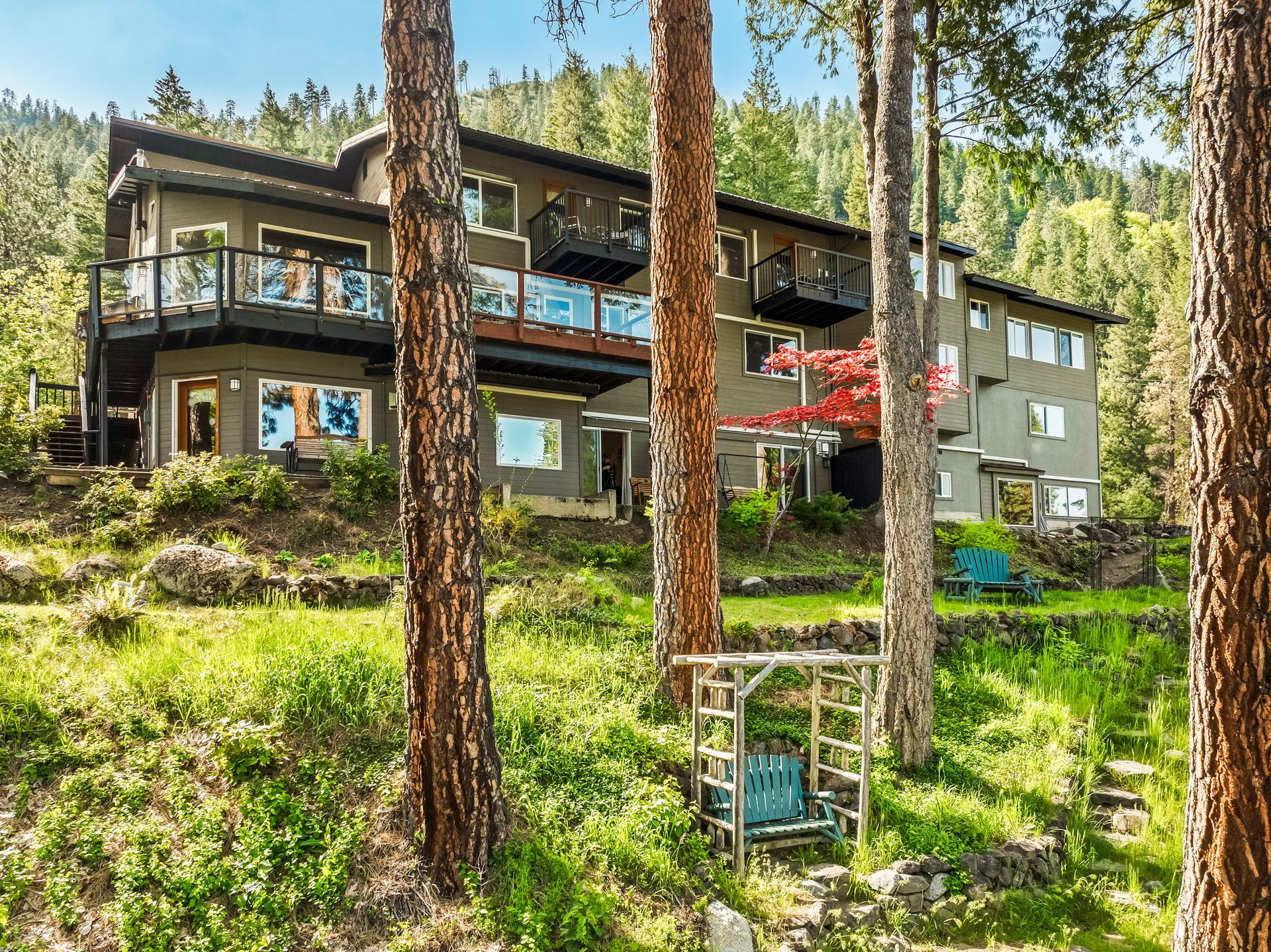 Boutique hotel in Leavenworth with balconies nestled in a hillside forest, surrounded by tall trees and lush green grass.