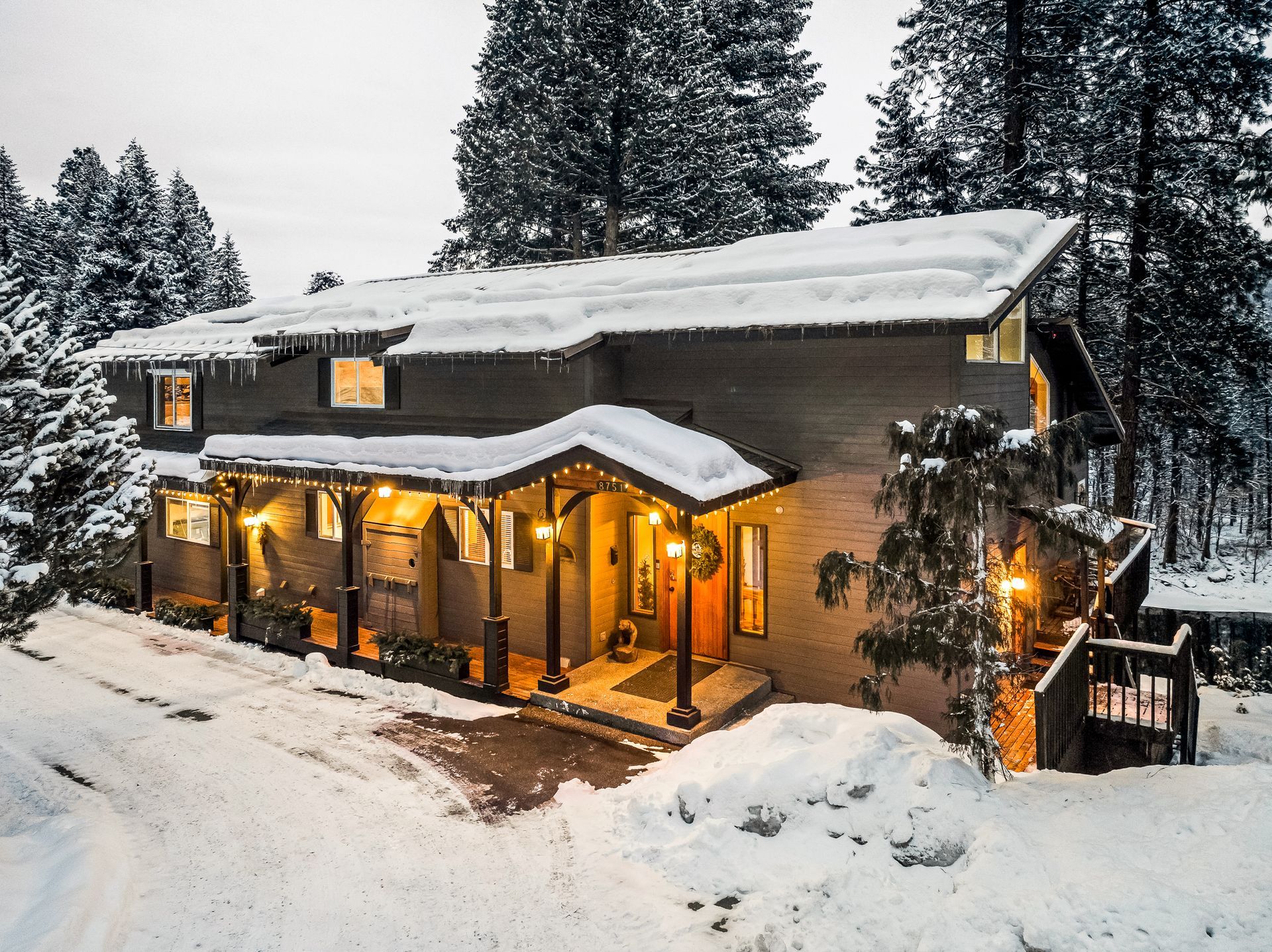 Snow-covered inn with porch lights on; surrounded by snow-covered trees and ground.