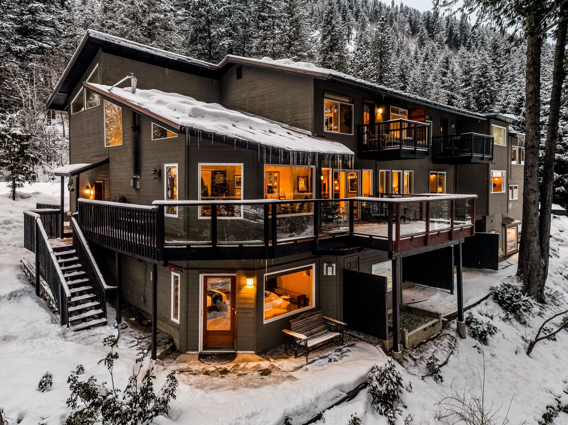 Boutique hotel in Leavenworth with snow-covered roof and deck, surrounded by snow-covered trees. Windows glow warmly.