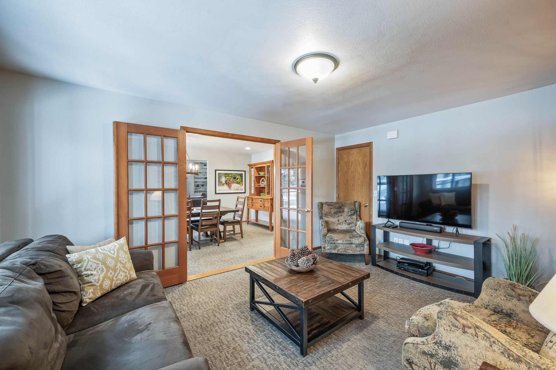 Living room with French doors to dining area, grey sofa, TV, and patterned armchair.