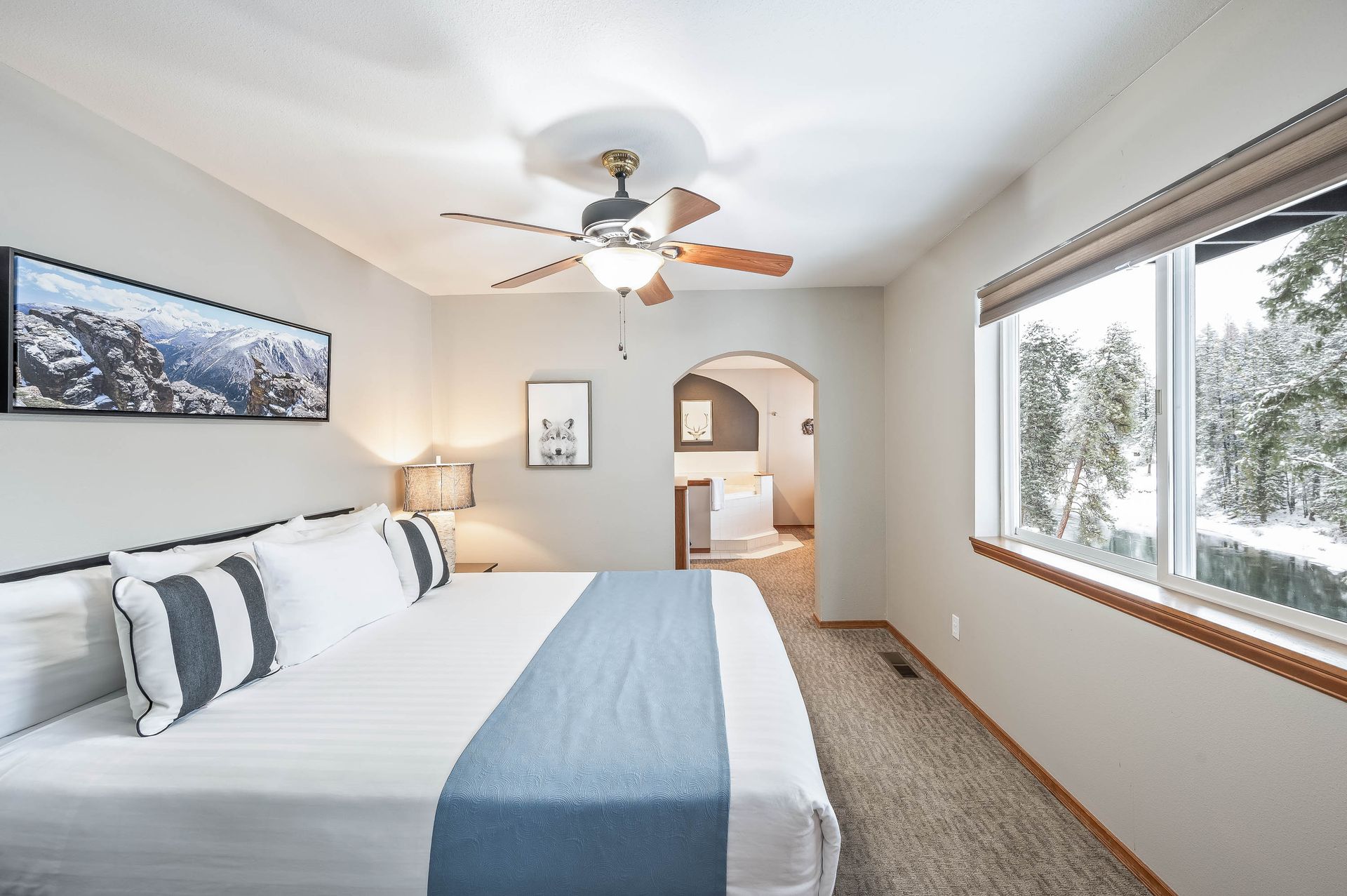 Bedroom with king-sized bed, snowy view from window, neutral tones, ceiling fan, archway to another room.