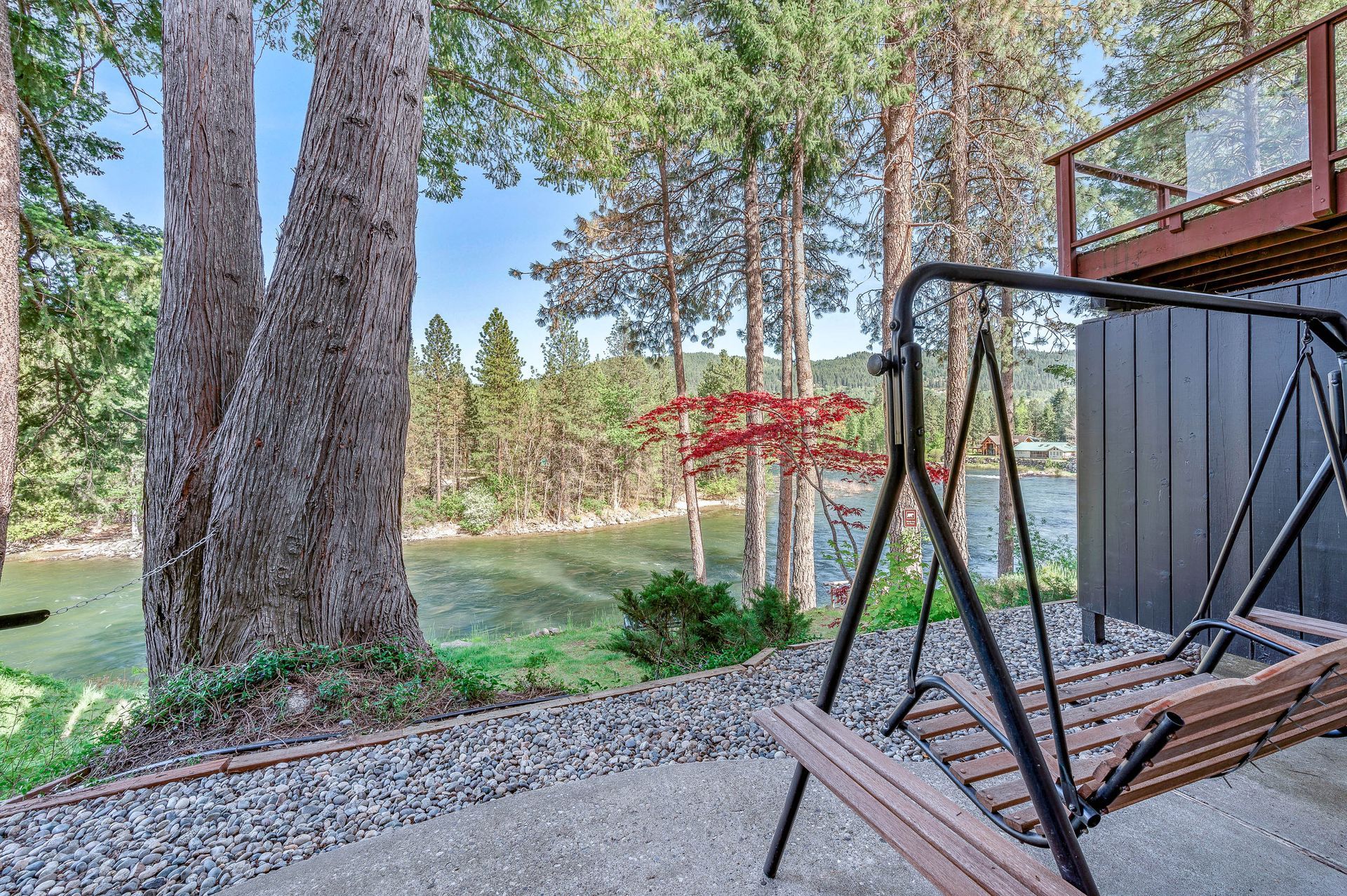 Patio with swing overlooking a river and trees.