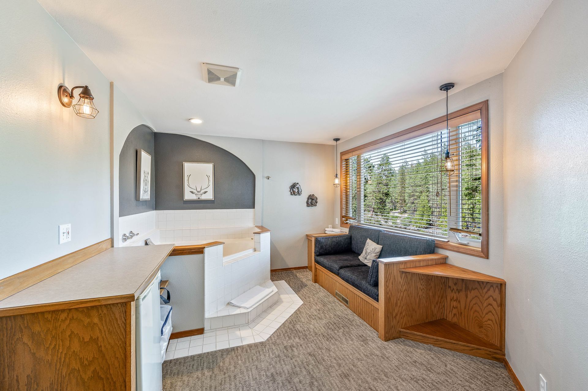 A cozy room with a jacuzzi, sofa, and large window overlooking trees.