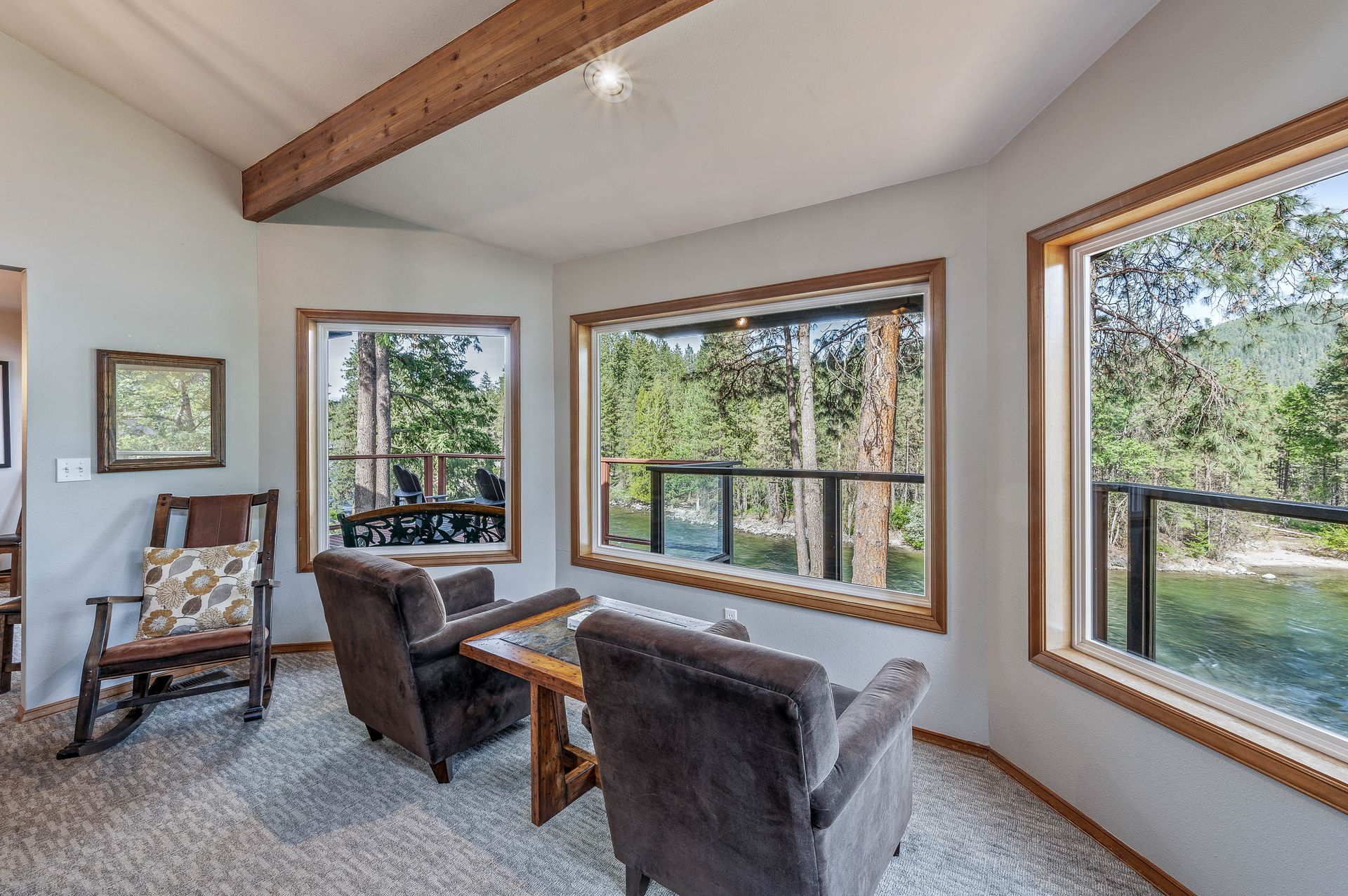 Bright living room with large windows, wood ceiling, and brown chairs overlooking a wooded view.