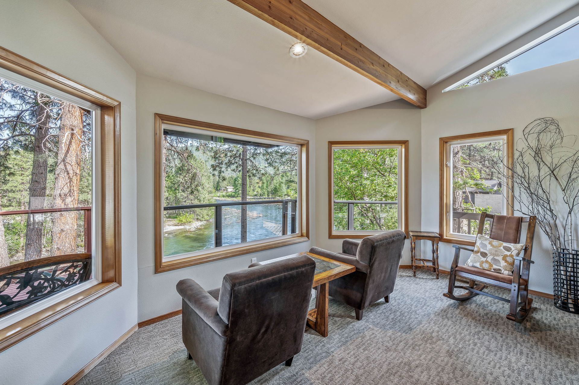 Sunroom with two armchairs, rocking chair, and large windows overlooking a river.