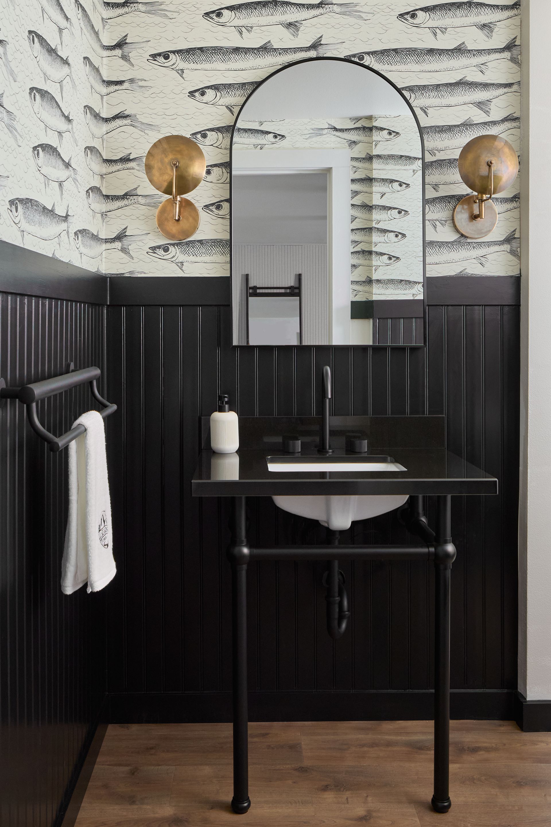 Small black-and-white bathroom vanity with arched mirror, wall sconces, and striped wallpaper