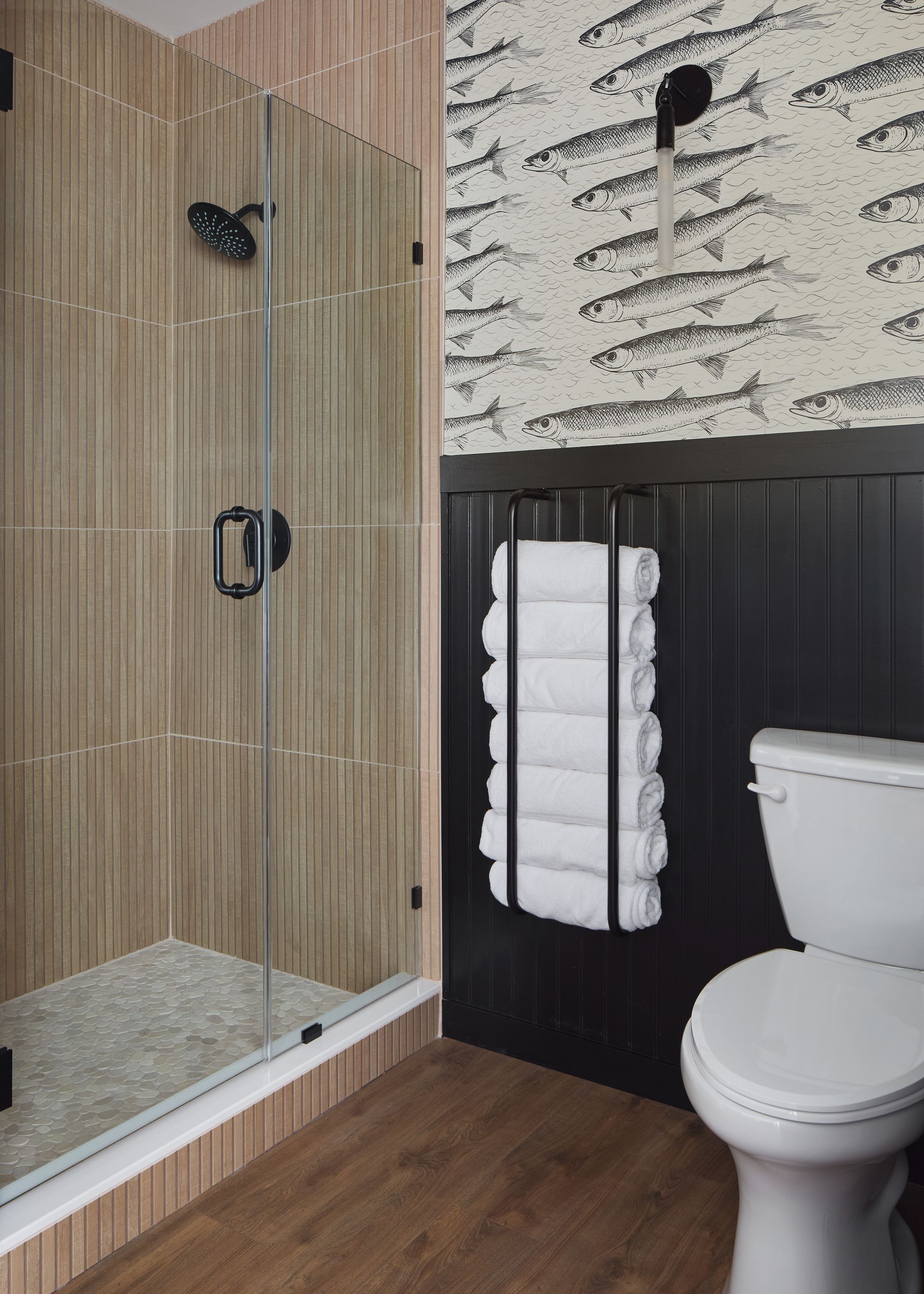 Bathroom with glass shower, black wainscoting, white toilet, and wood-look floor