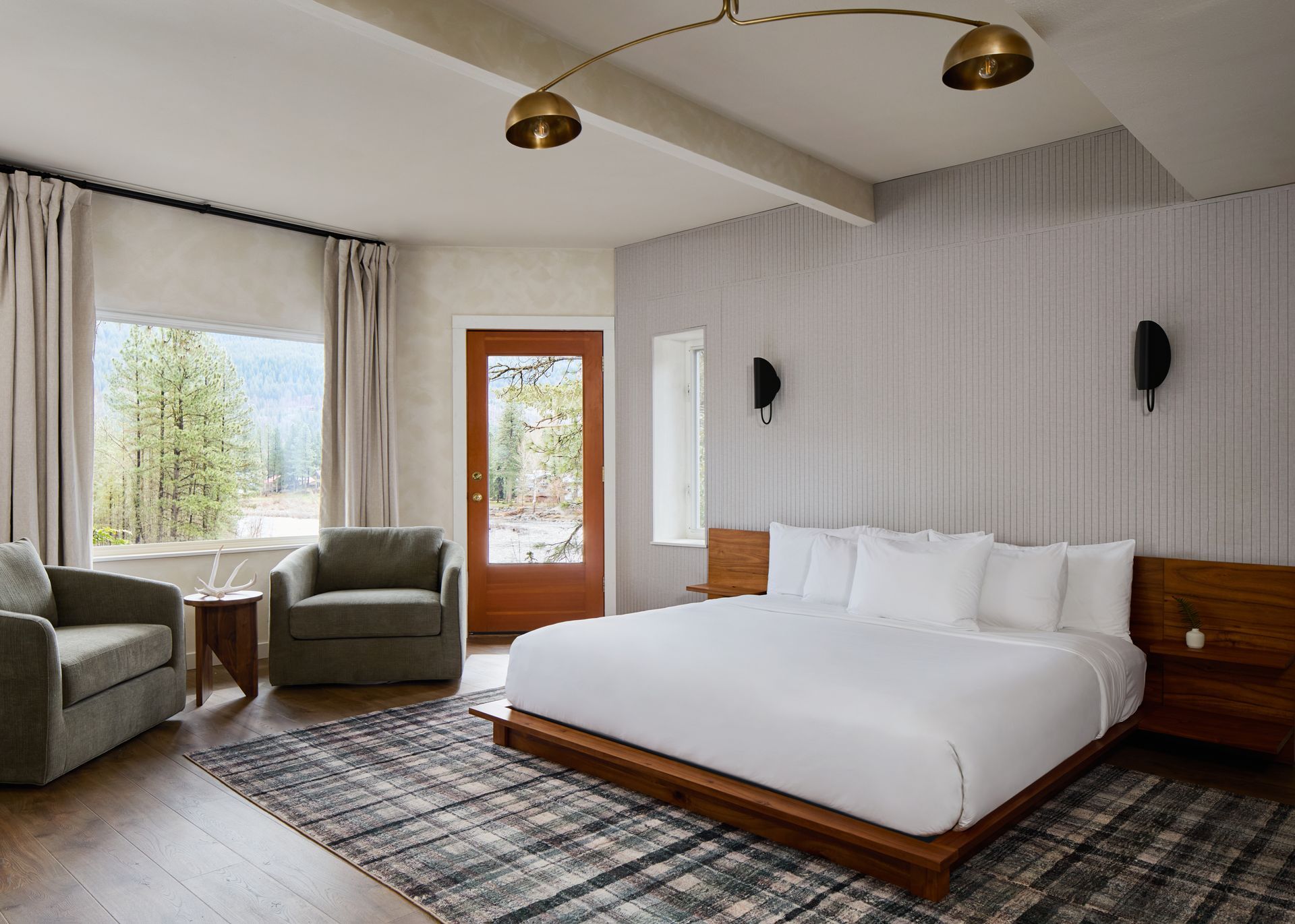 Modern bedroom with king bed, gray armchairs, wood accents, and a large window overlooking snowy trees
