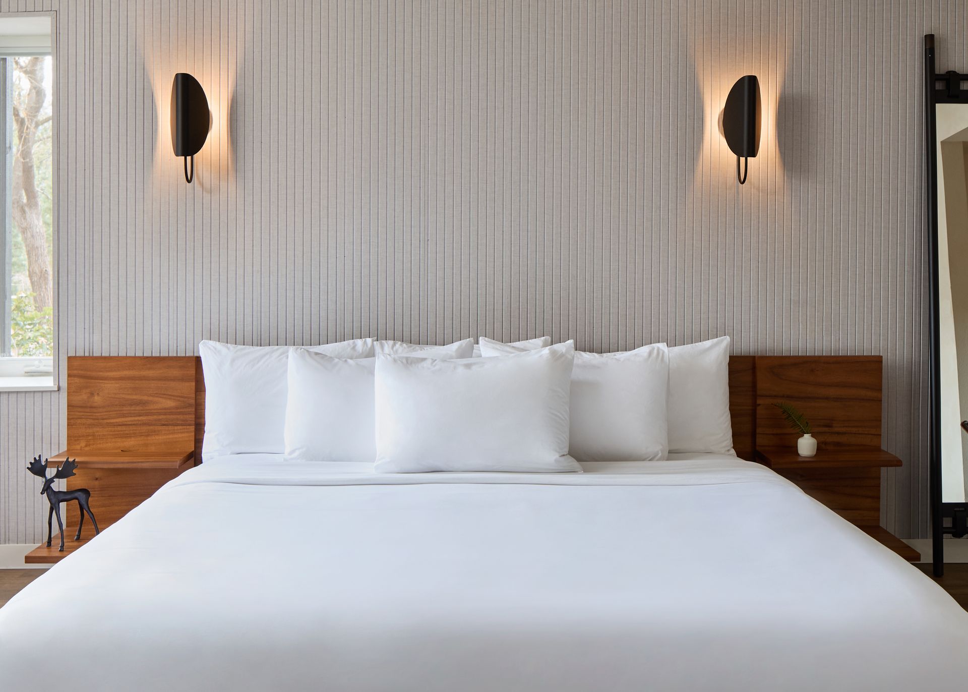 Modern bedroom with a large white bed, wood headboard, and wall sconces on textured wallpaper