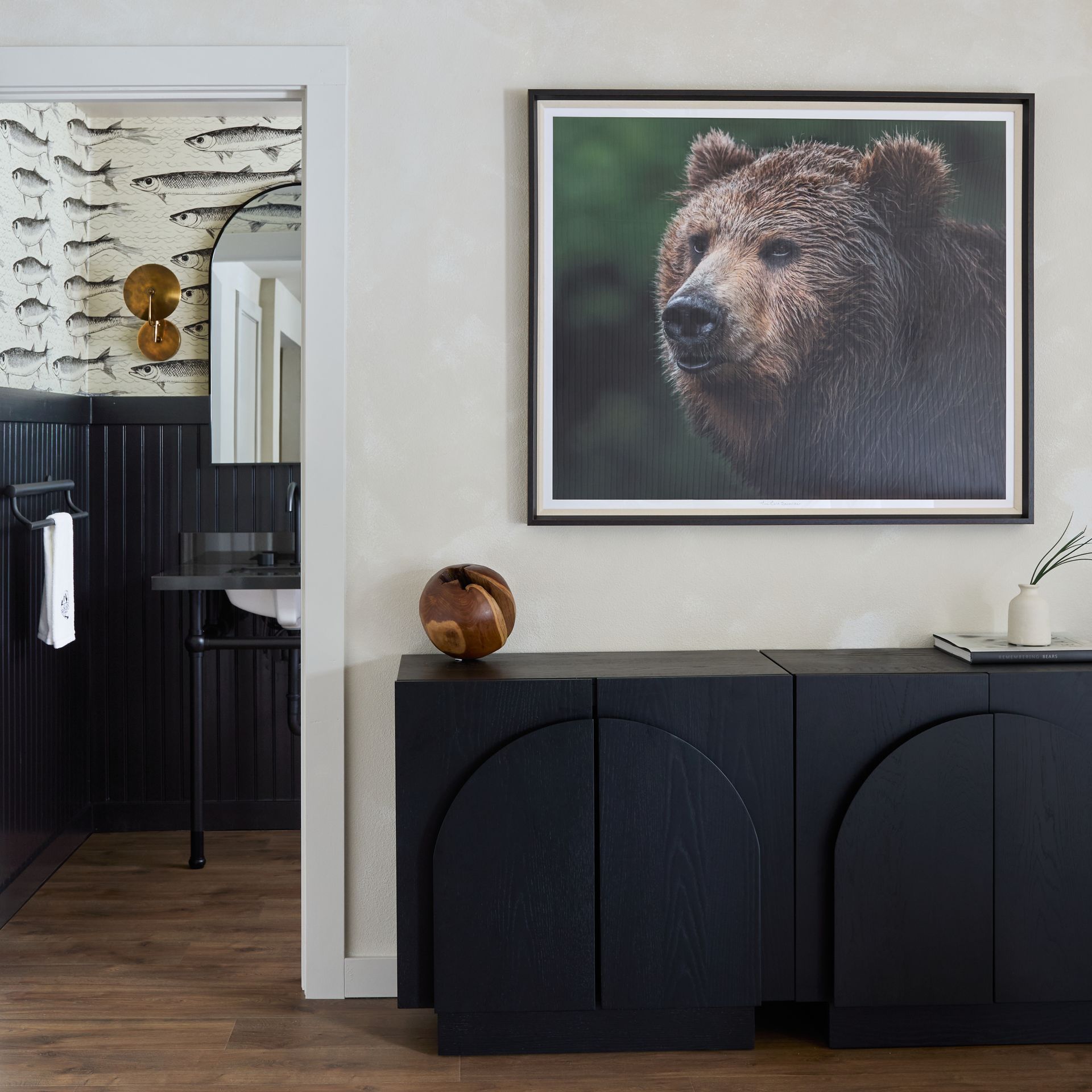 Framed bear portrait above a dark cabinet in a modern hallway with a black-and-white patterned doorway.