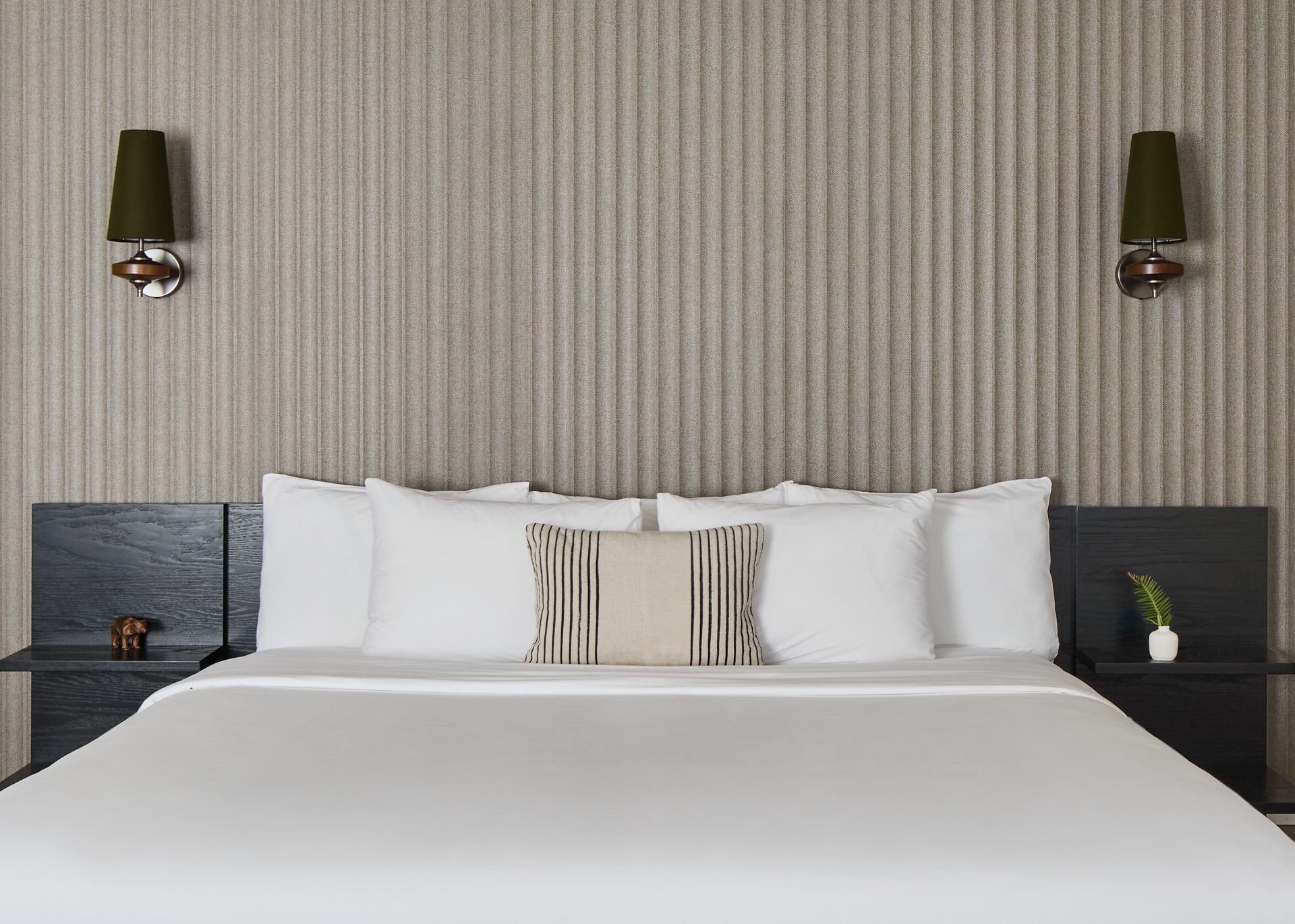 Neatly made hotel bed with white linens, striped headboard wall, and dark bedside tables with lamps