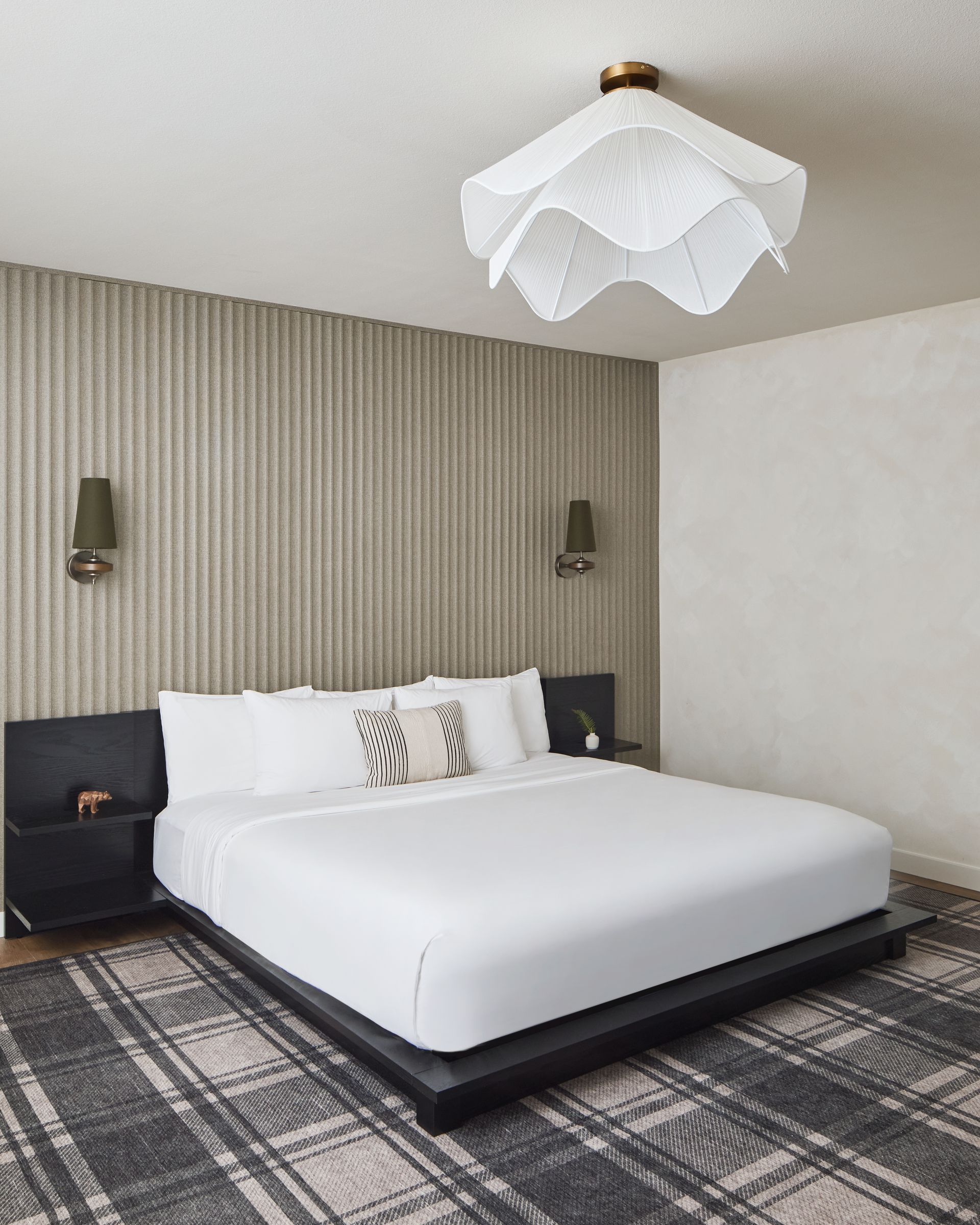Modern bedroom with white bed, black nightstands, striped accent wall, and geometric pendant light.