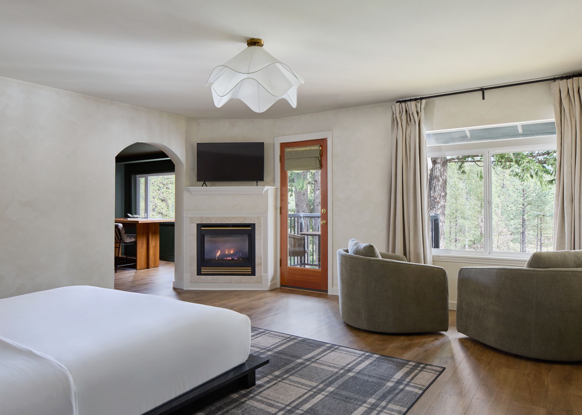 Bright bedroom with fireplace, large window, bed, and two chairs overlooking trees