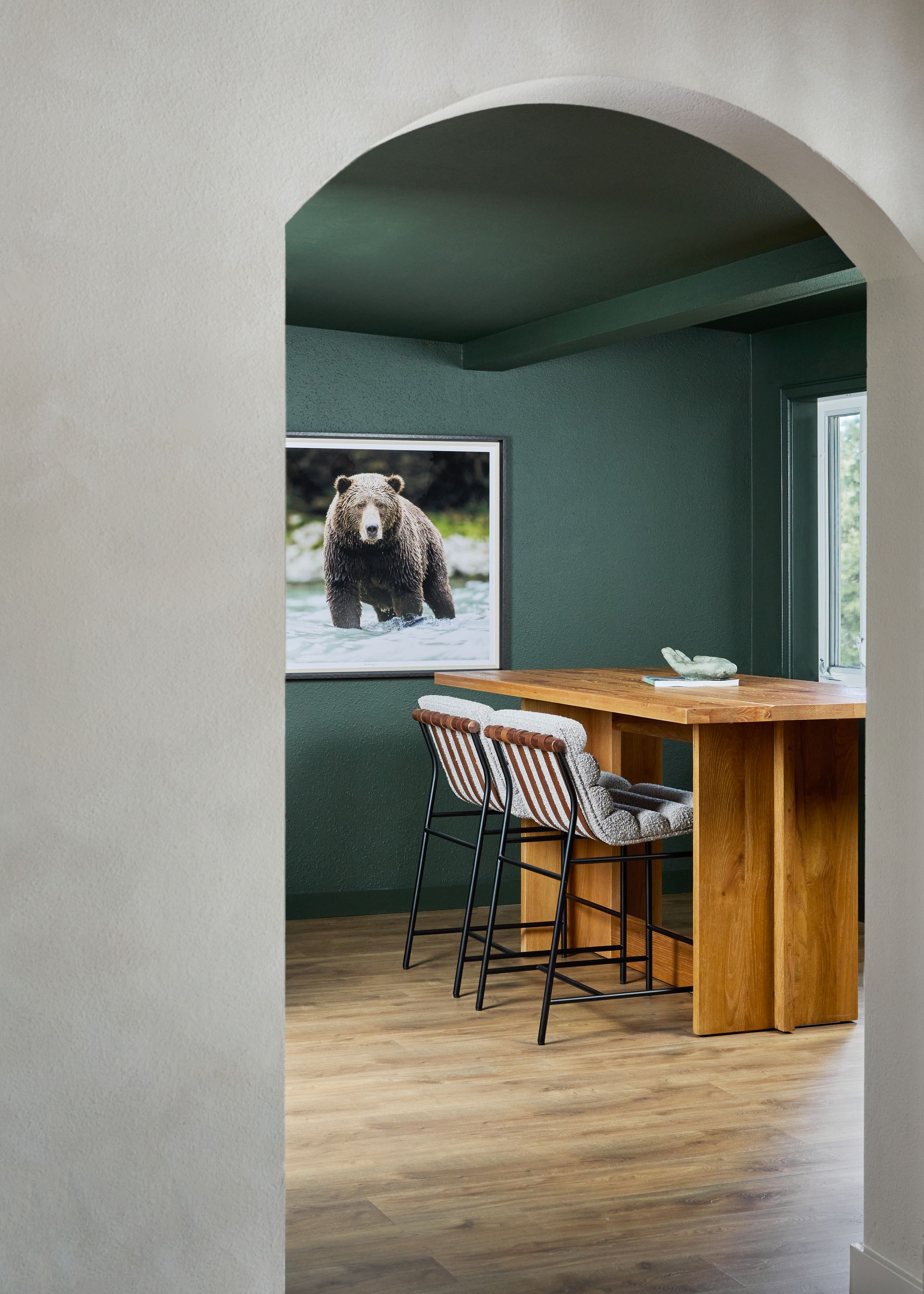 Archway view into teal dining room with wooden table, two stools, and bear artwork on the wall