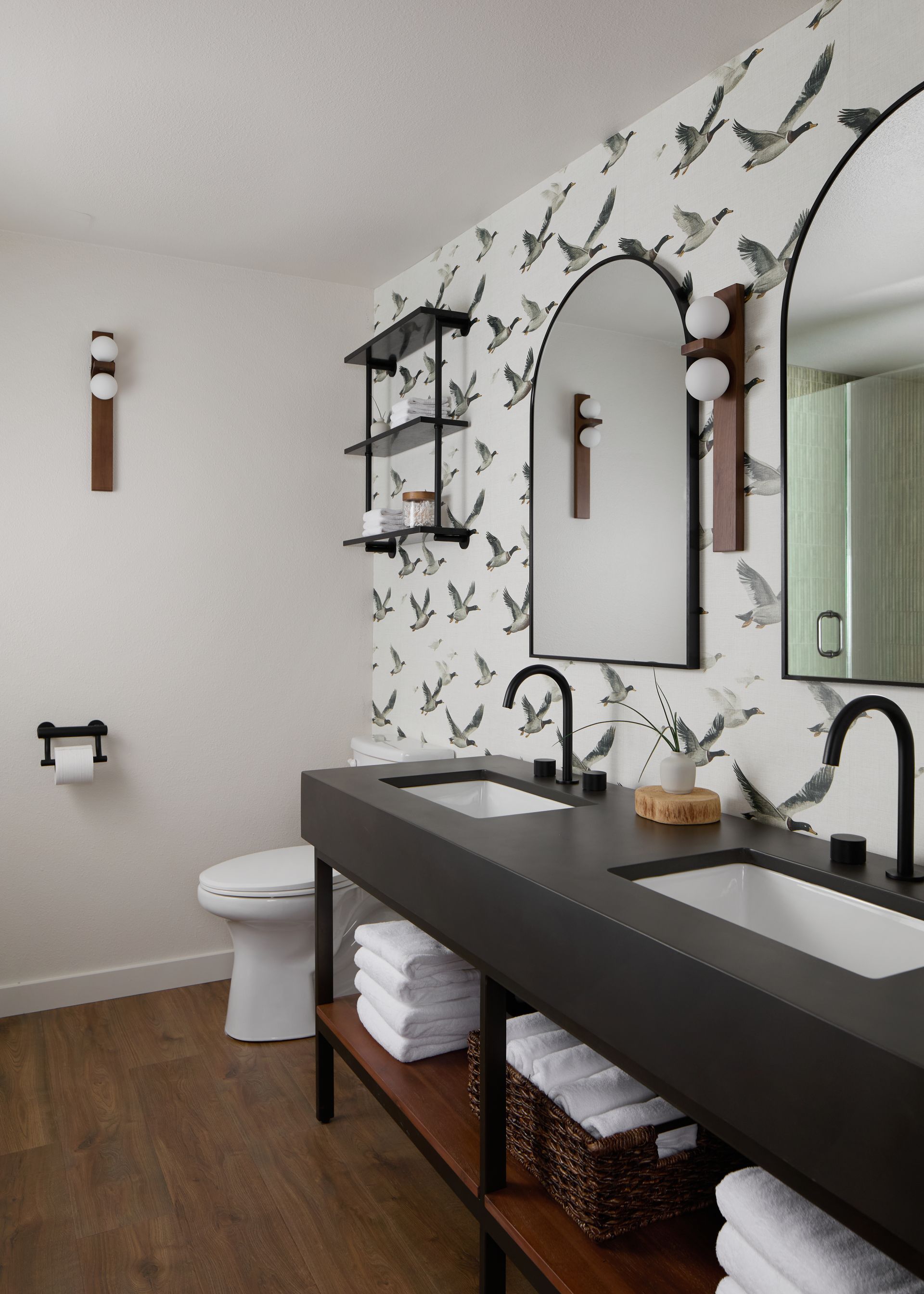 Modern bathroom with black double vanity, mirrors, butterfly wallpaper, and toilet on the left