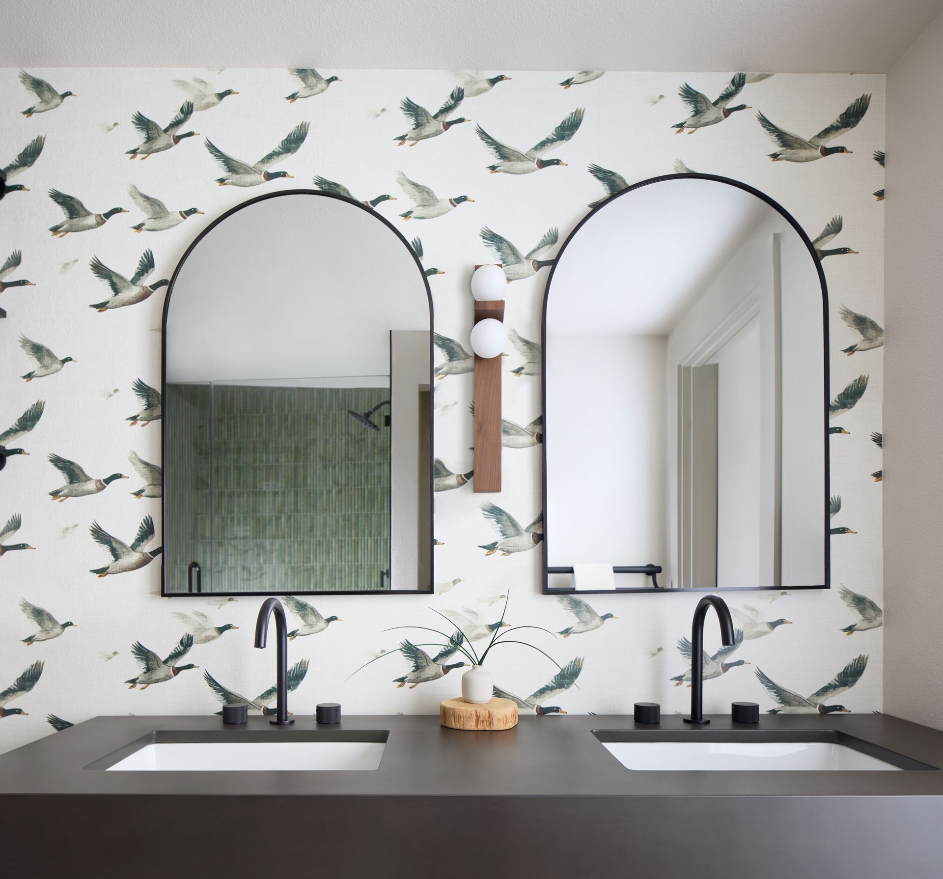 Double vanity bathroom with arched mirrors, floral wallpaper, and dark countertops