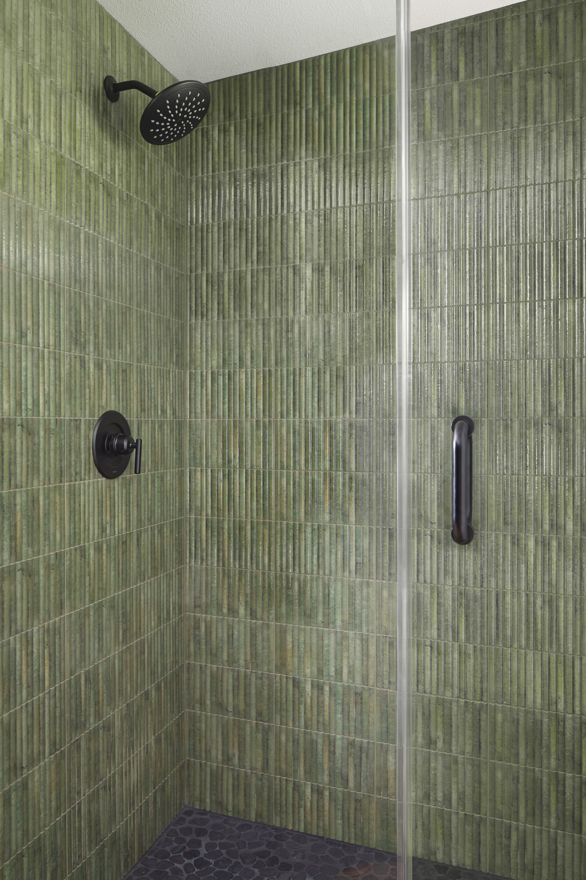 Green-tiled shower with glass door, black fixtures, and dark shower bench