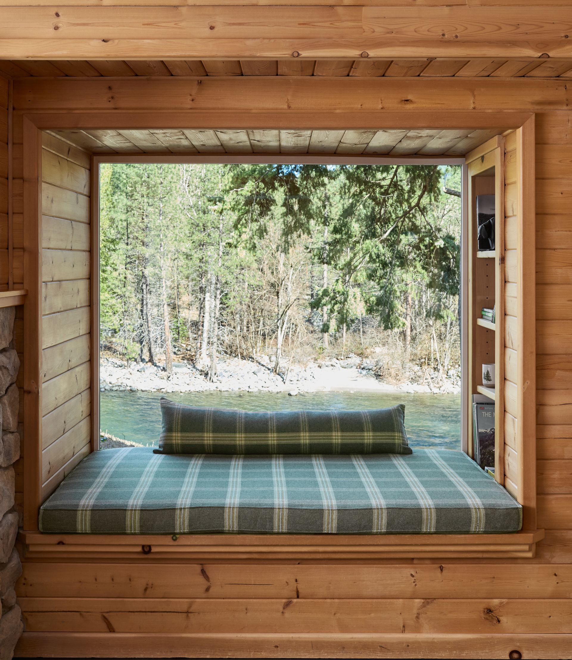 Wooden window seat with green plaid cushion, overlooking a forest and lake outside.