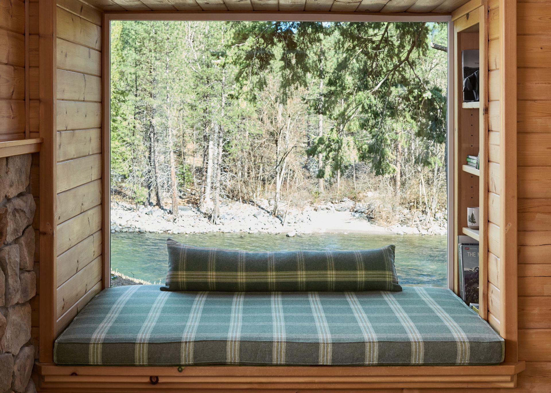 Wooden cabin window seat with striped cushion overlooking a forest and lake