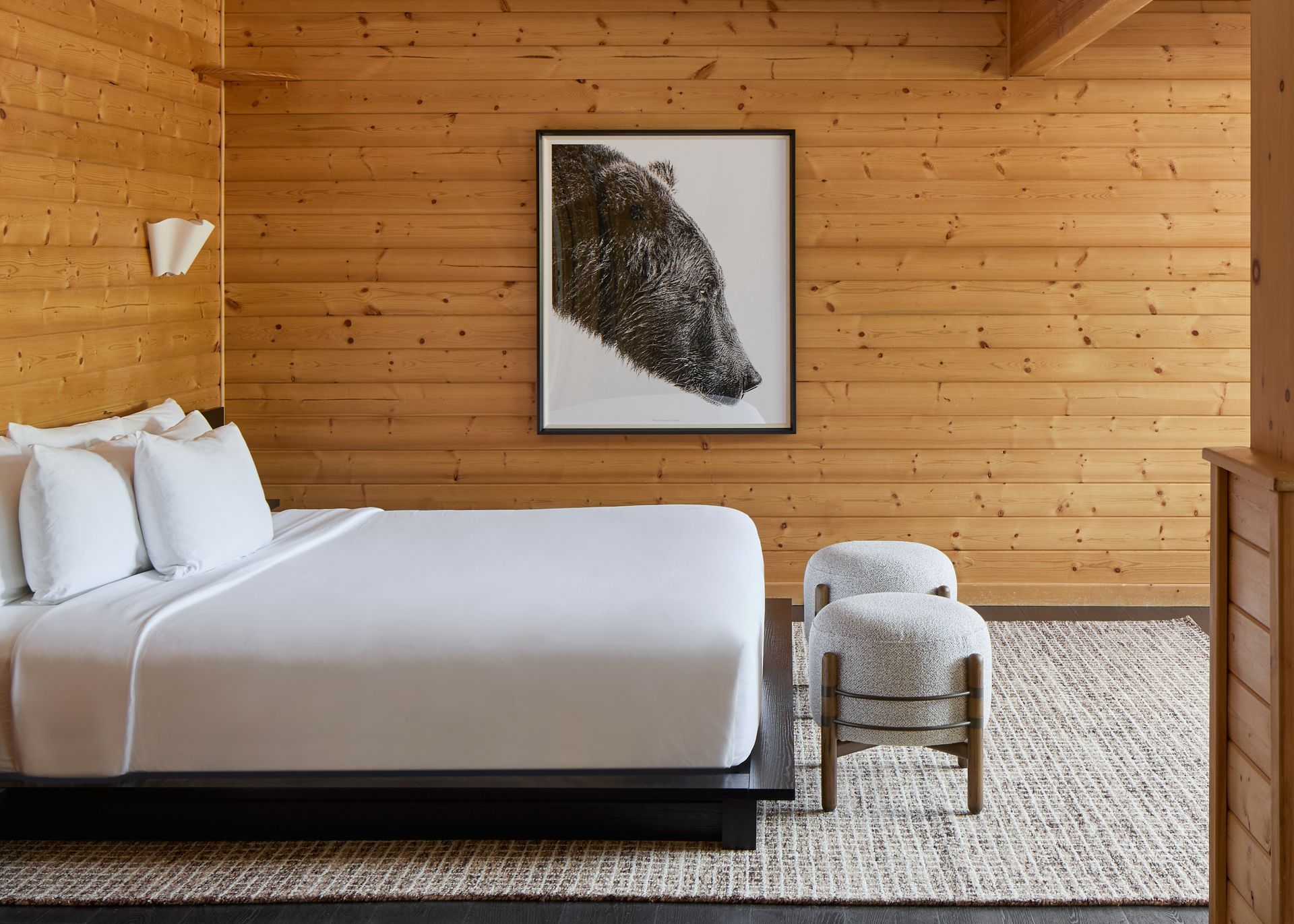 Minimalist bedroom with wood walls, white bed, framed artwork, and woven rug
