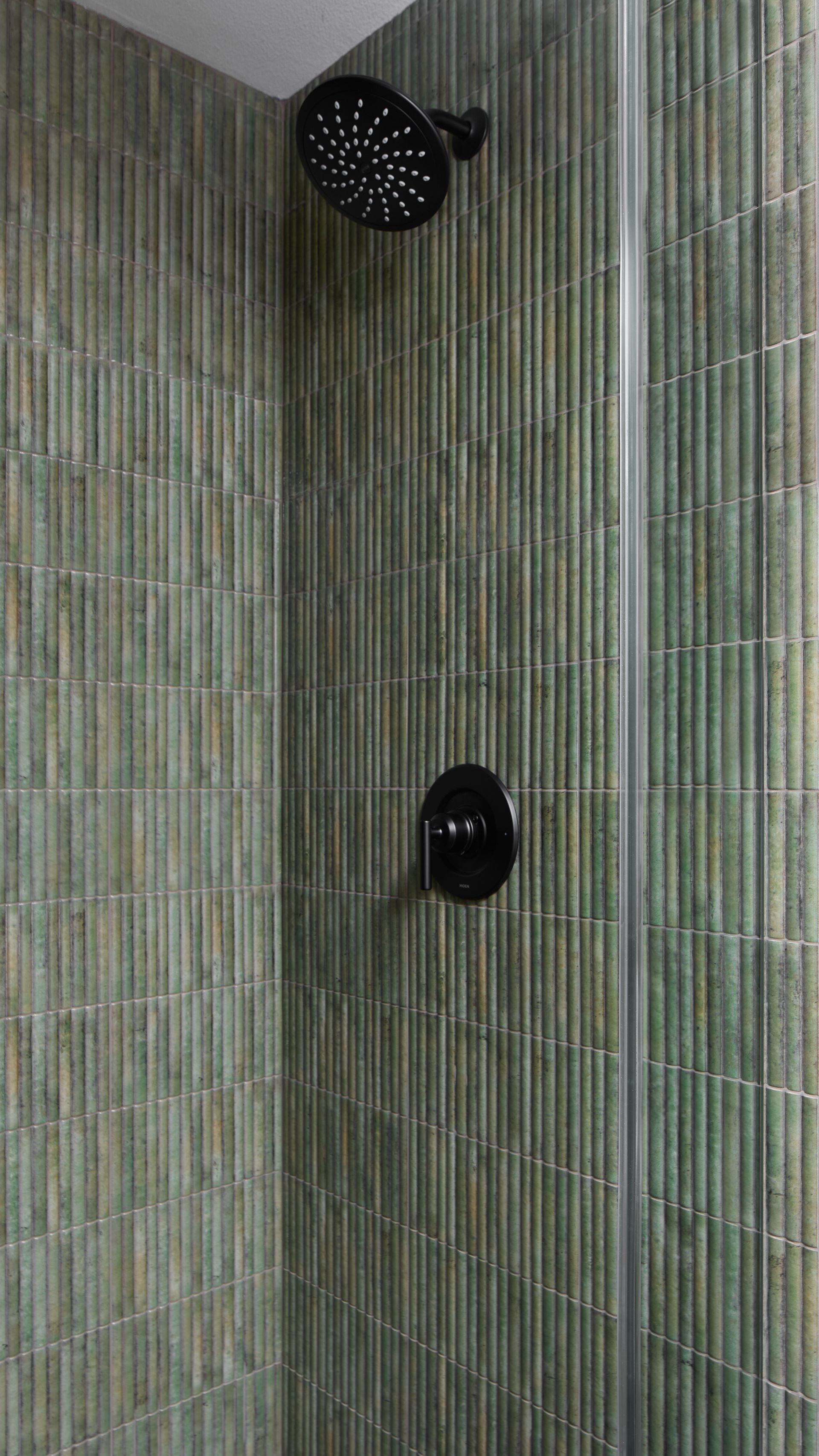 Modern shower corner with green tile walls and two black shower fixtures