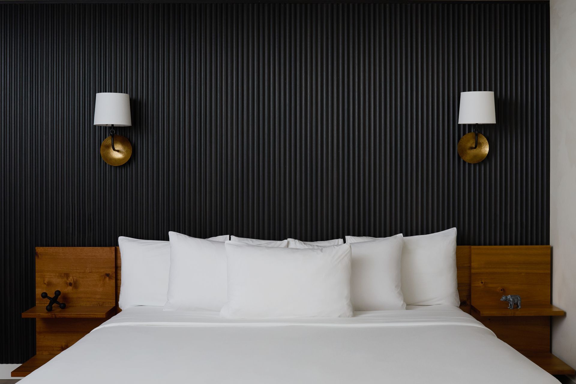 Modern bedroom with a large white bed, wooden headboards, and black striped wall with two lamps