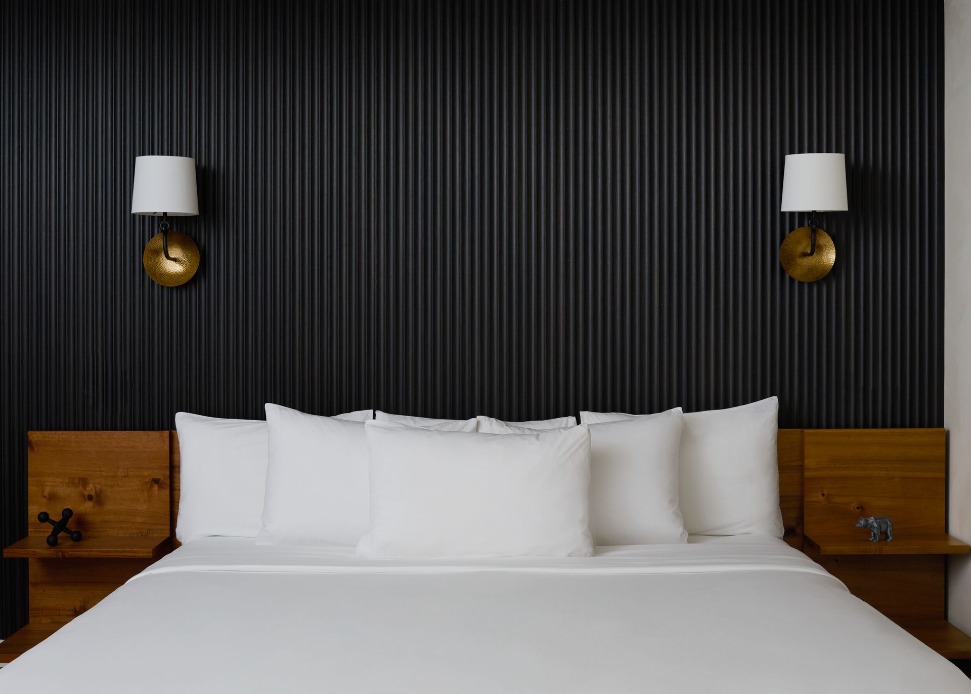 Modern bedroom with a large bed, white bedding, black paneled wall, and matching bedside lamps