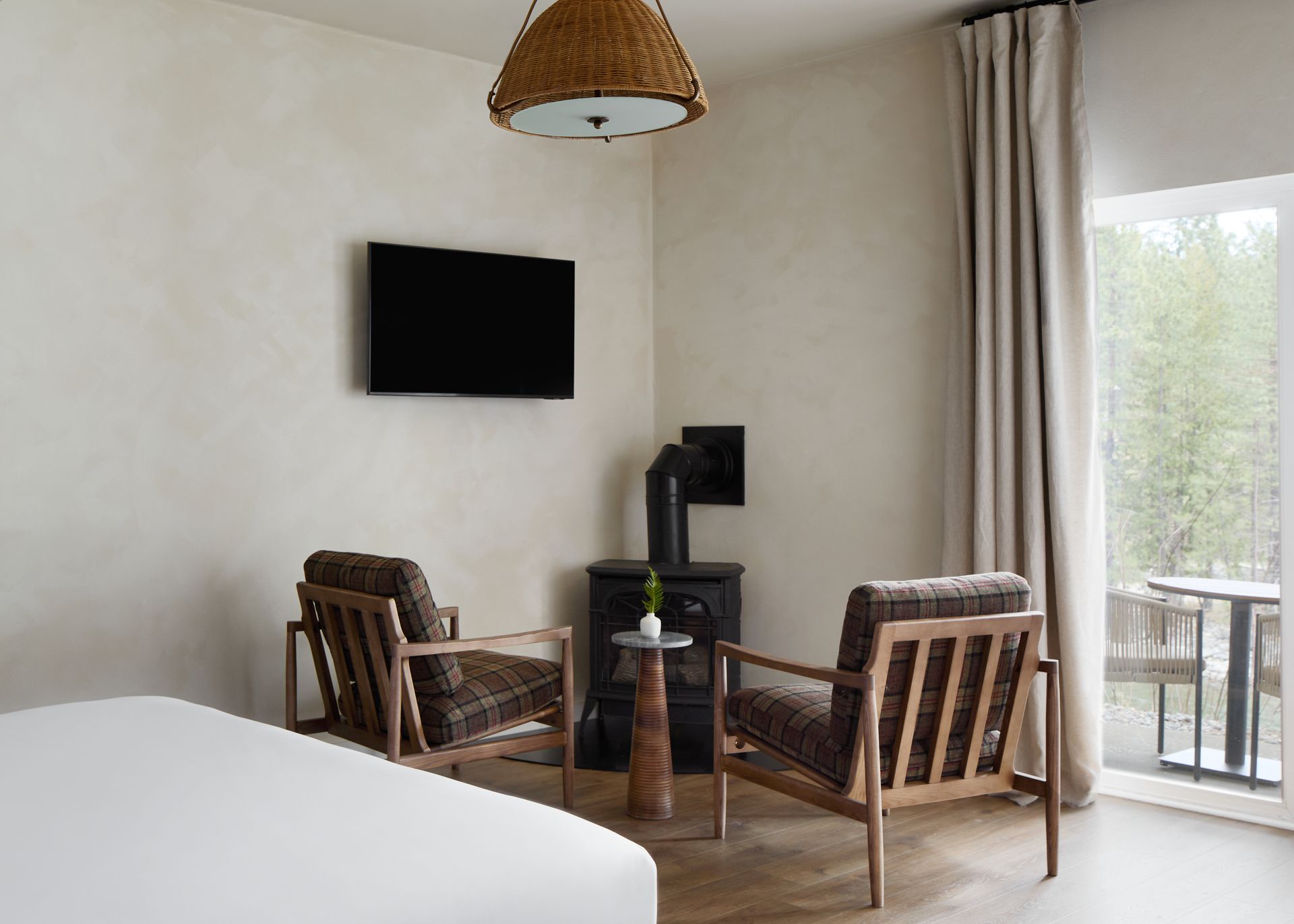Modern bedroom with two wooden chairs, wall-mounted TV, and sliding glass door to a balcony
