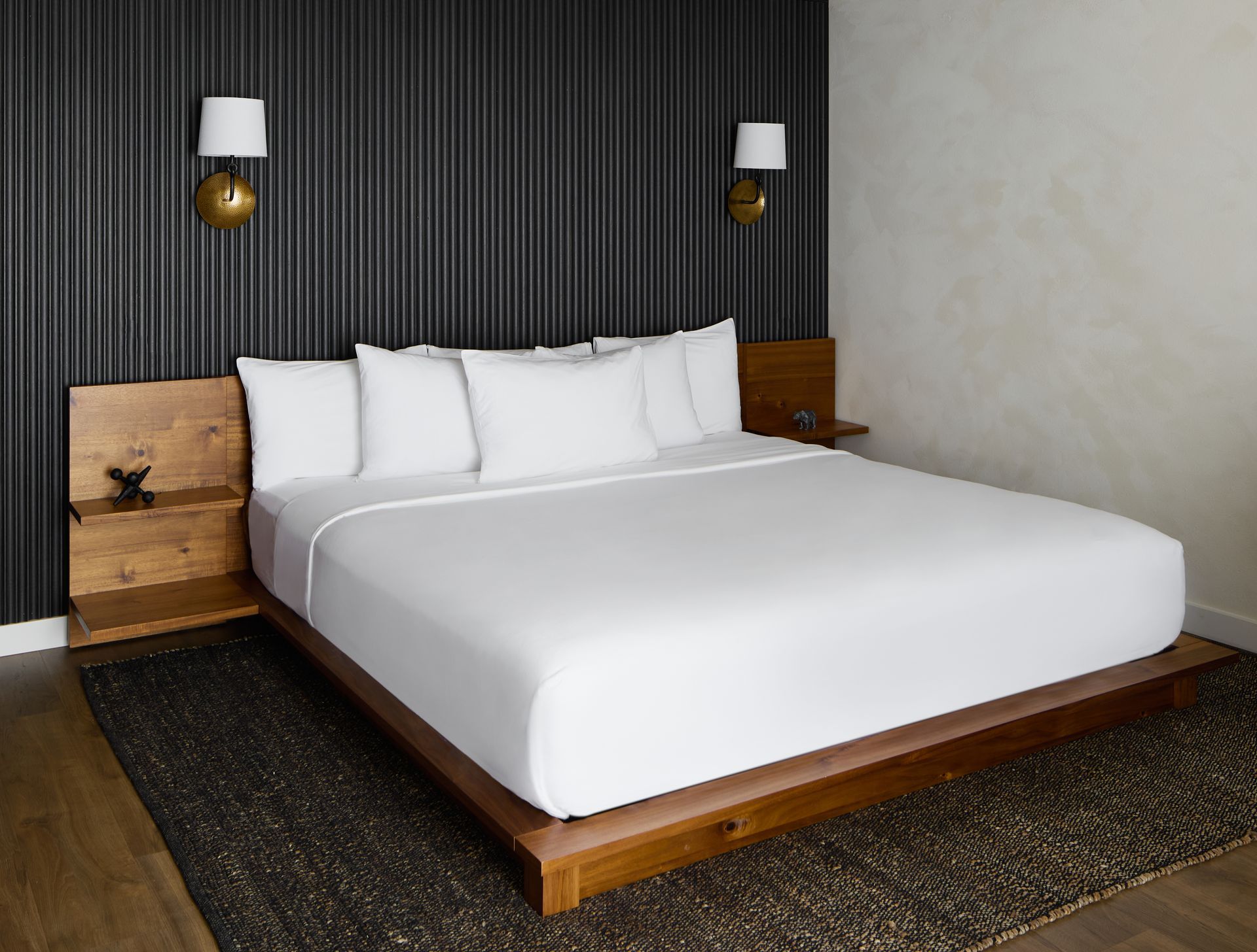 Modern bedroom with a white bed, wooden headboard, dark curtains, and wall sconces