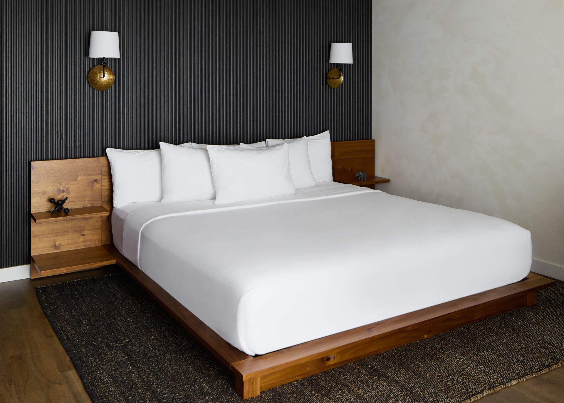 Modern bedroom with a wooden platform bed, white bedding, and dark textured walls