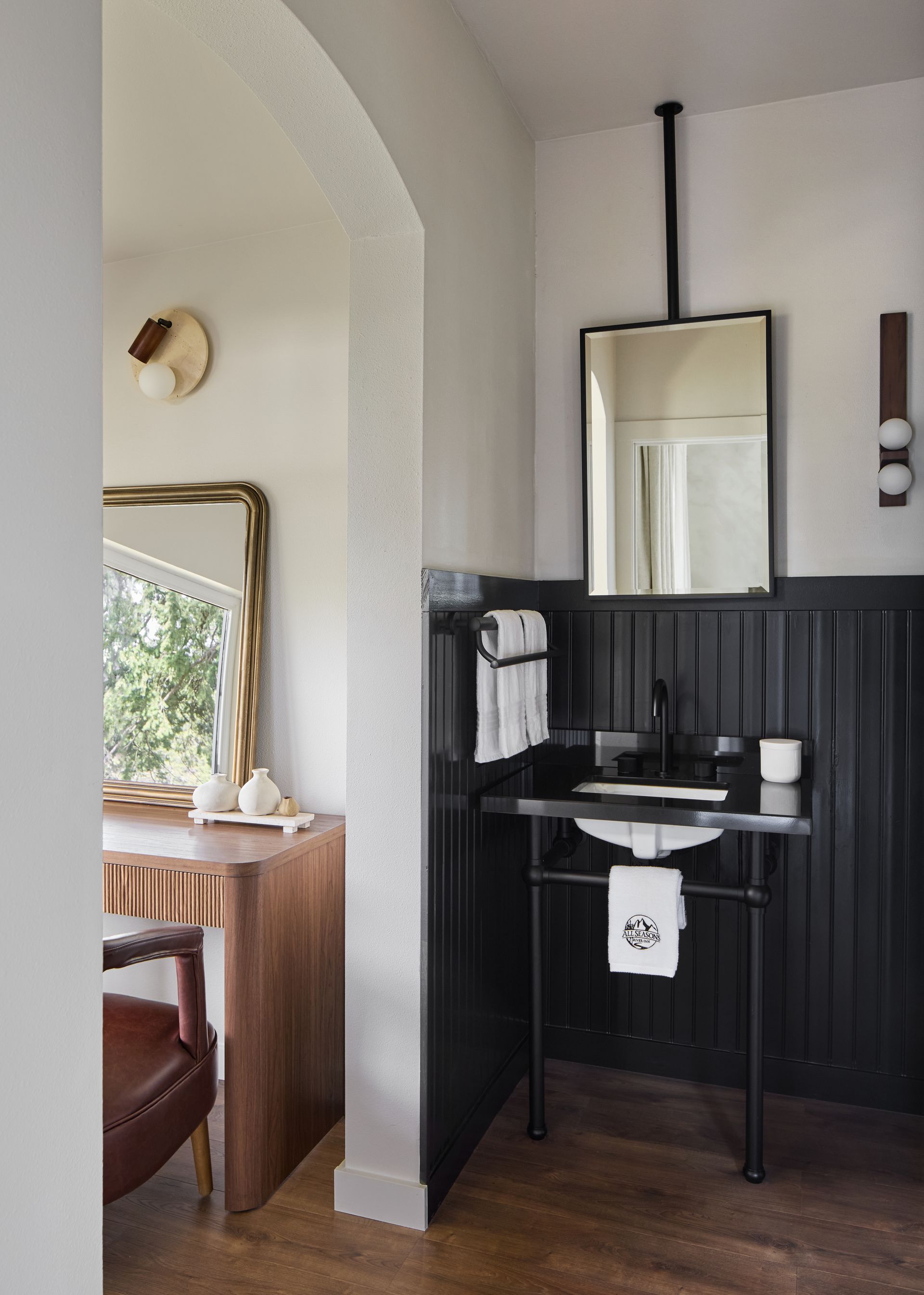 Small bathroom vanity with black wall paneling, mirror, sink, towel, and a doorway to a bedroom.