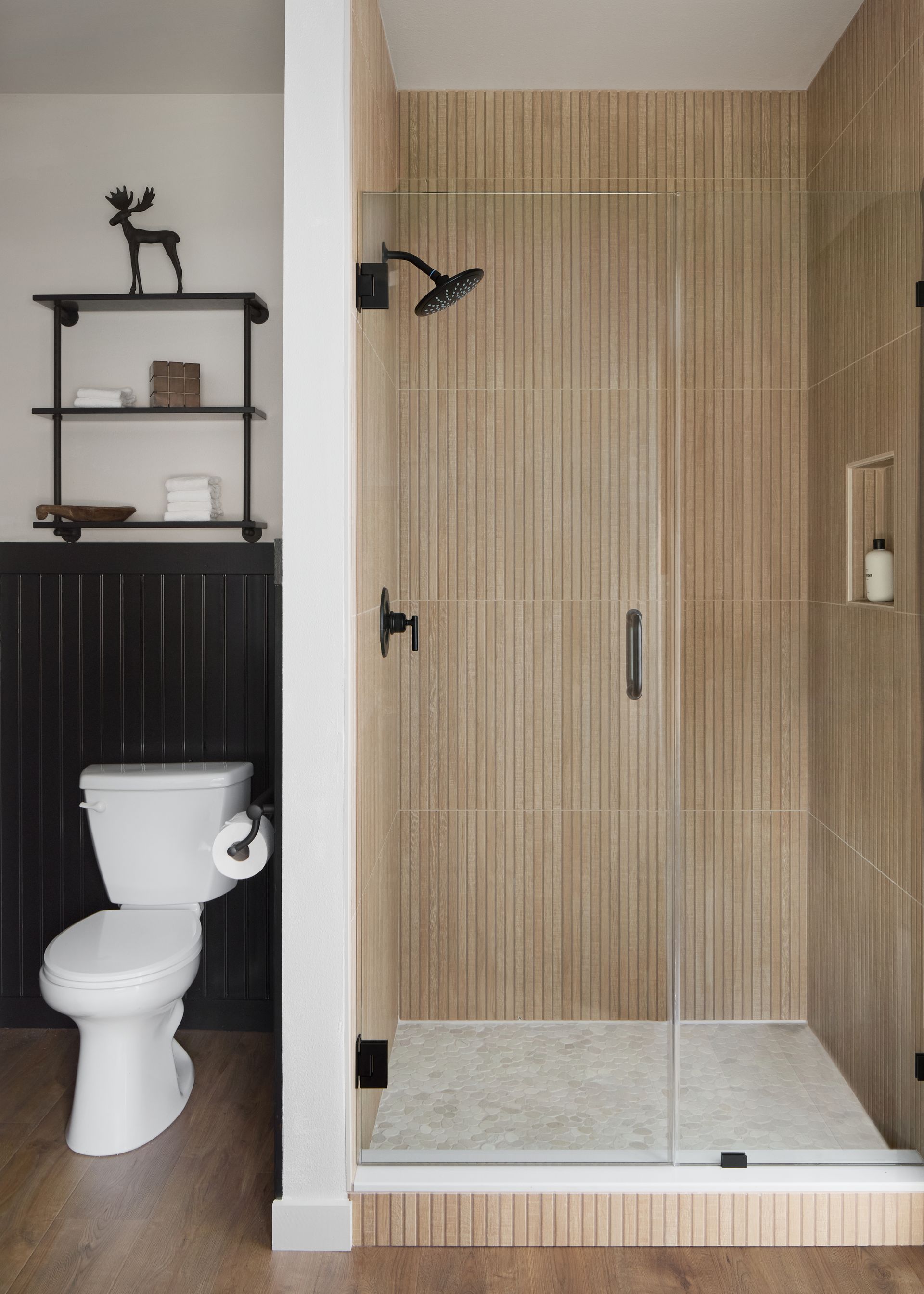 Modern bathroom with a glass shower, light wood slat walls, and a white toilet on the left.