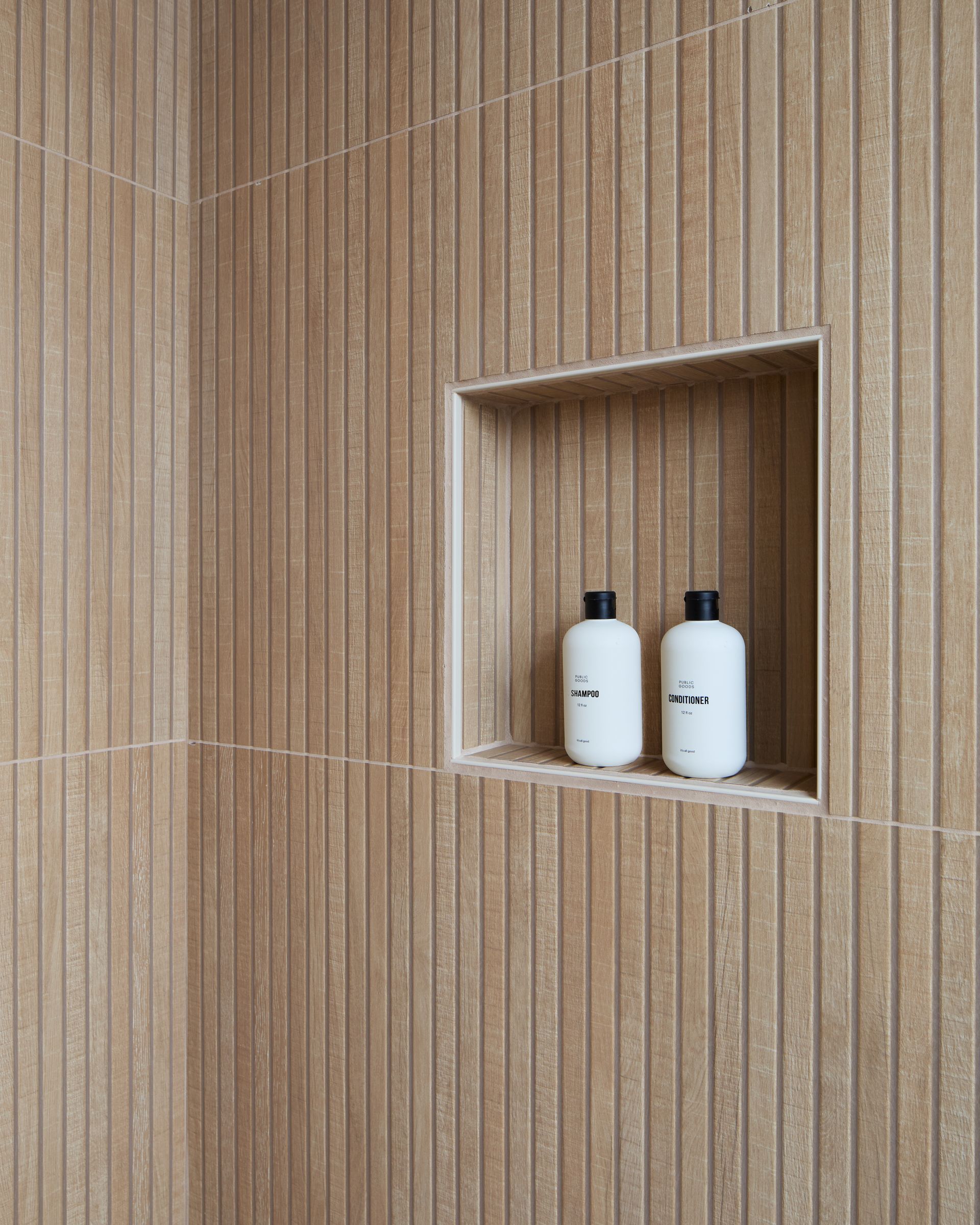 Two white bottles in a recessed wall shelf against beige tiled walls.