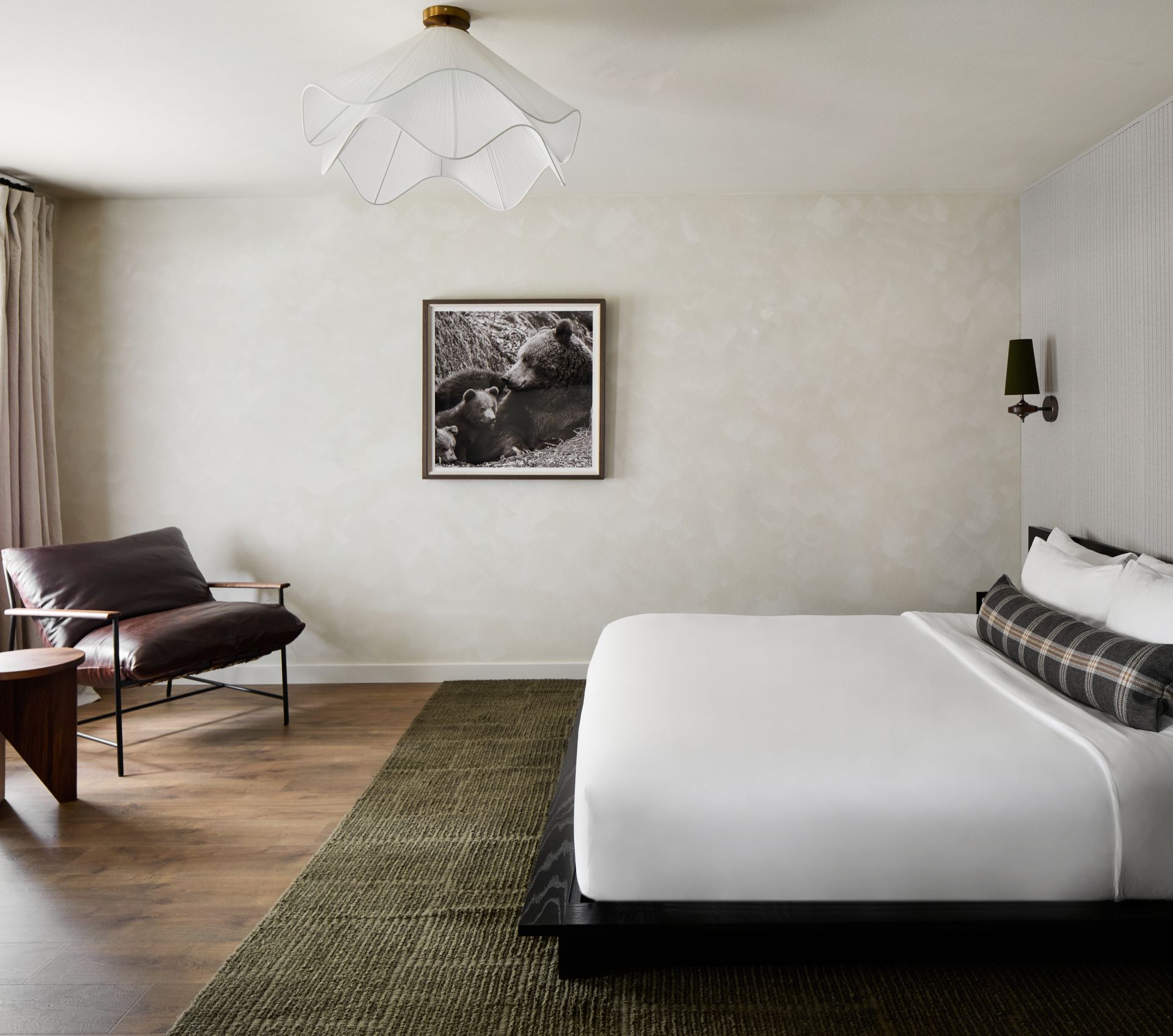 Modern bedroom with white bed, green rug, wooden floor, chair, and framed wall art