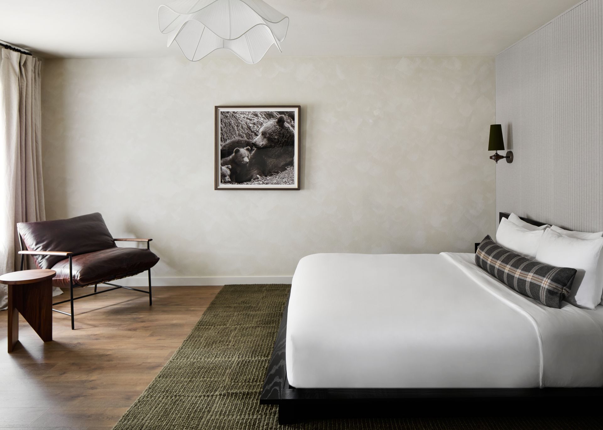 Modern bedroom with a large bed, chair, side table, wall art, and soft neutral decor