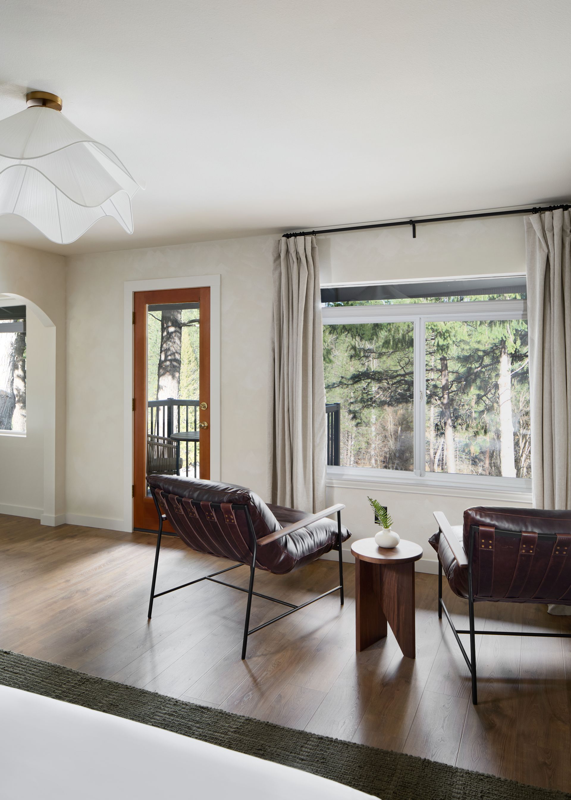 Bright living room with two chairs, small table, and large windows overlooking greenery