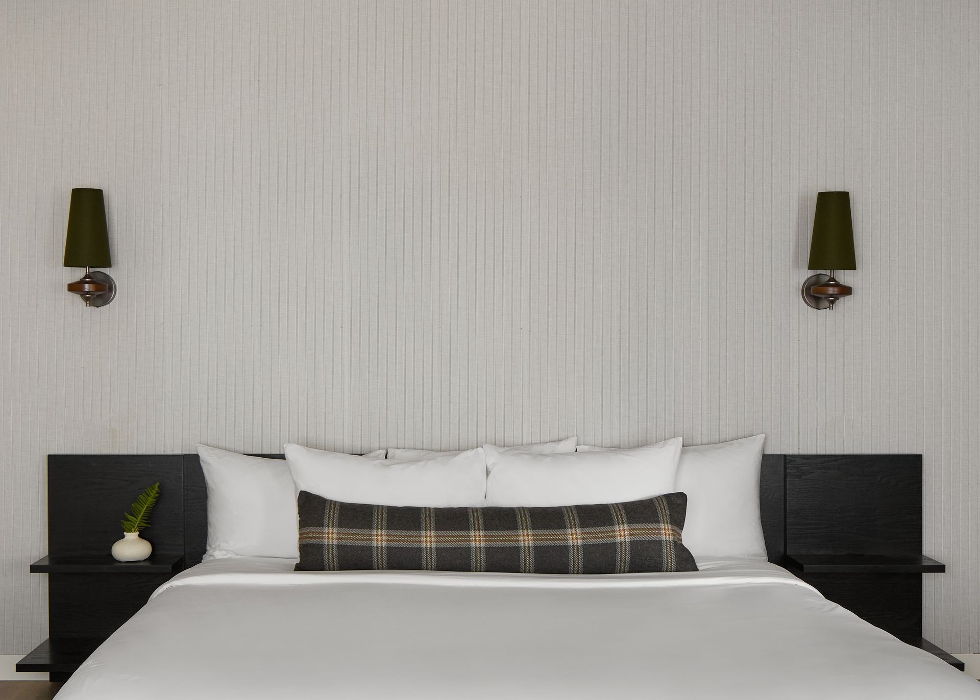 Modern hotel room with a neatly made bed, black headboards, and wall sconces