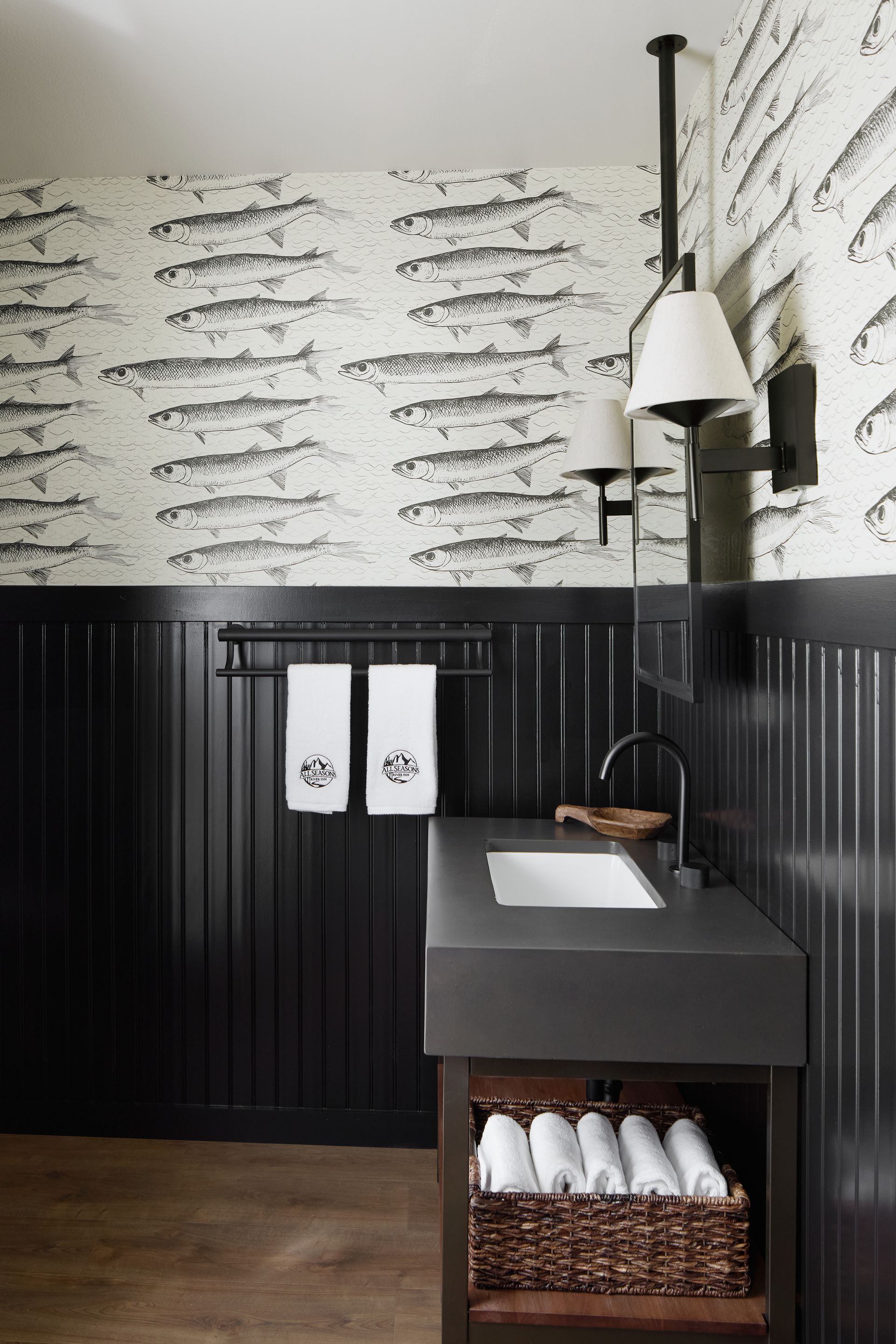 Modern bathroom with black wainscoting, fish-pattern wallpaper, sink, mirror, and woven towel basket