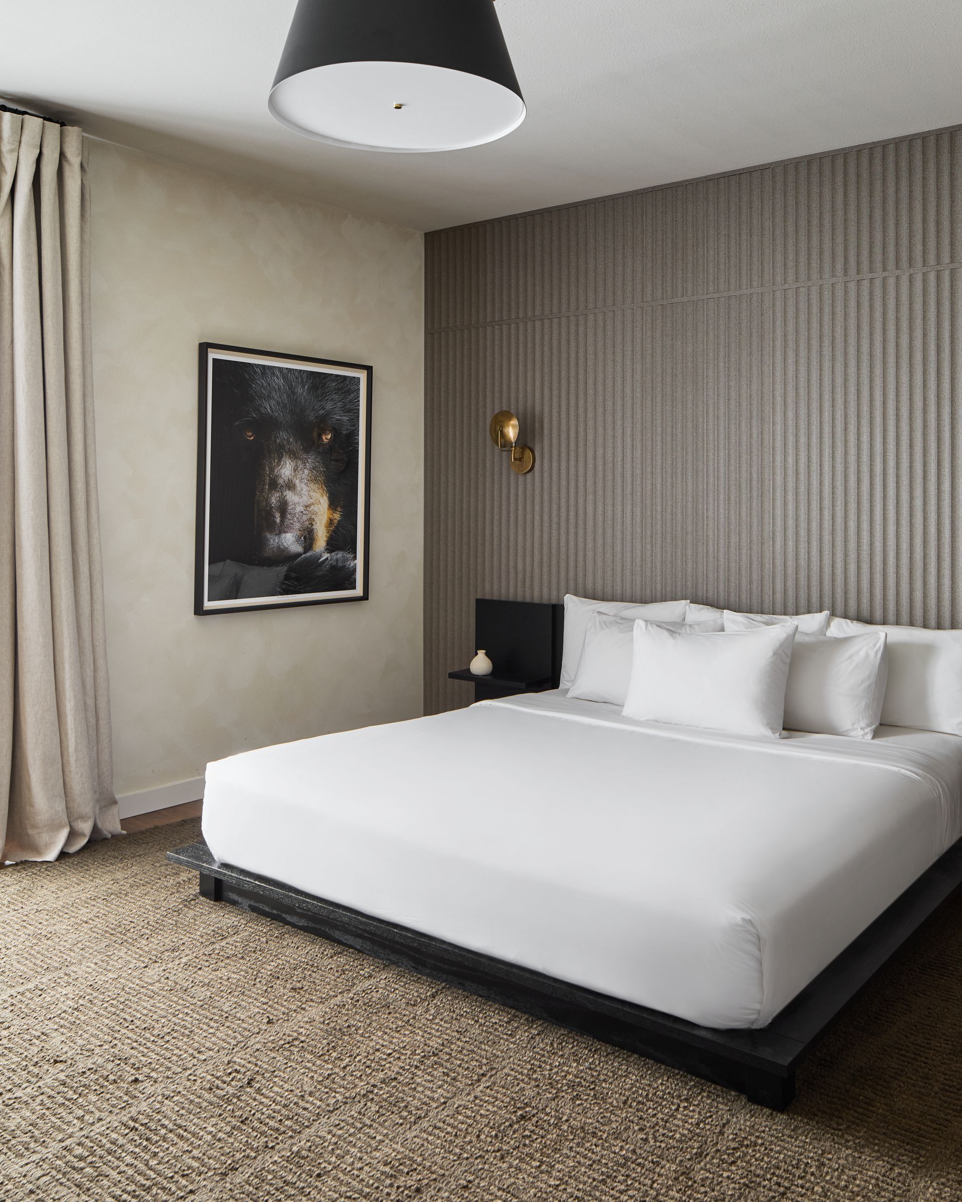 Modern bedroom with a white bed, textured wall, framed art, and a hanging ceiling lamp.